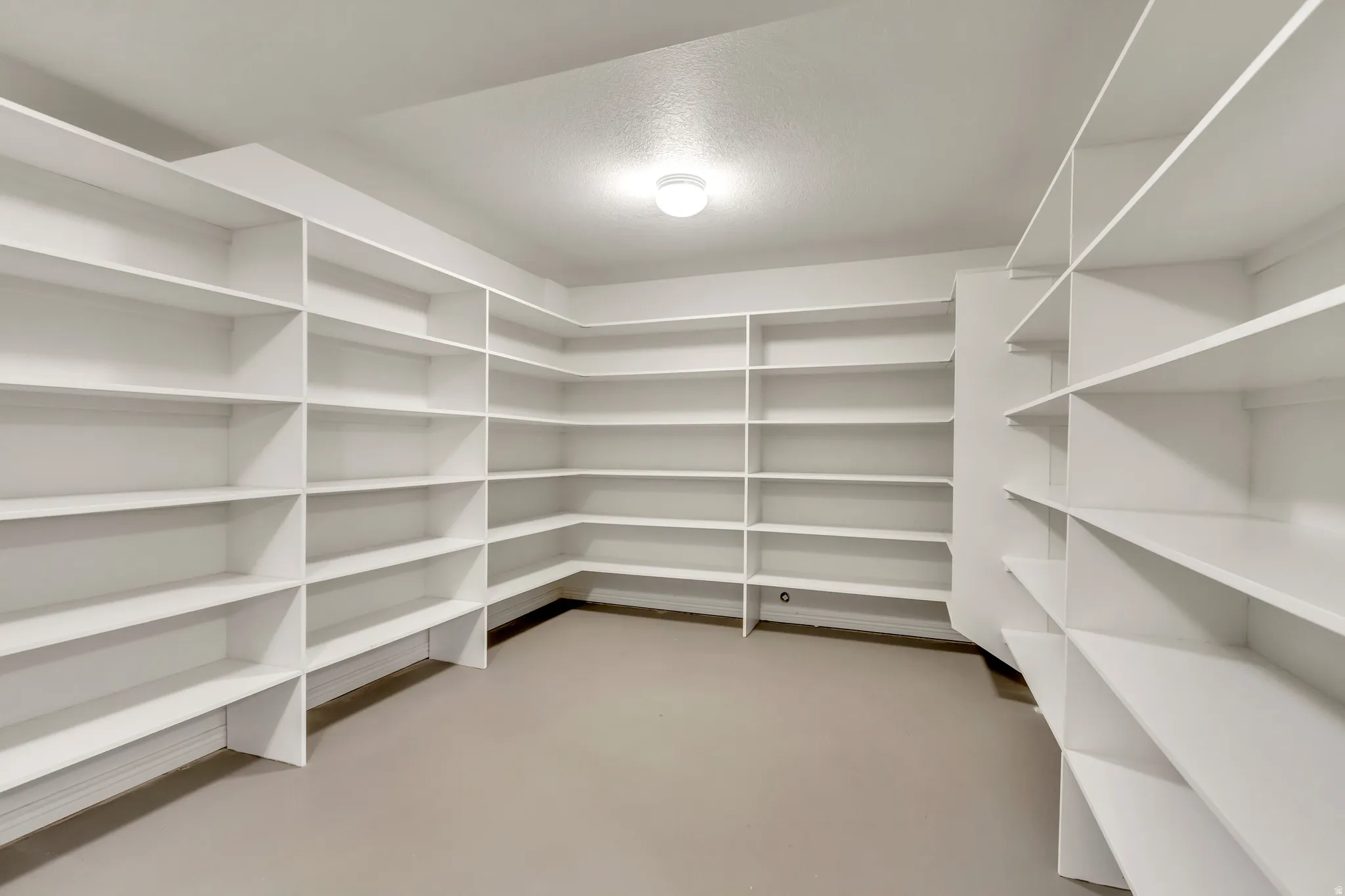 Spacious walk-in pantry featuring extensive white built-in shelving, ample storage options, and overhead lighting