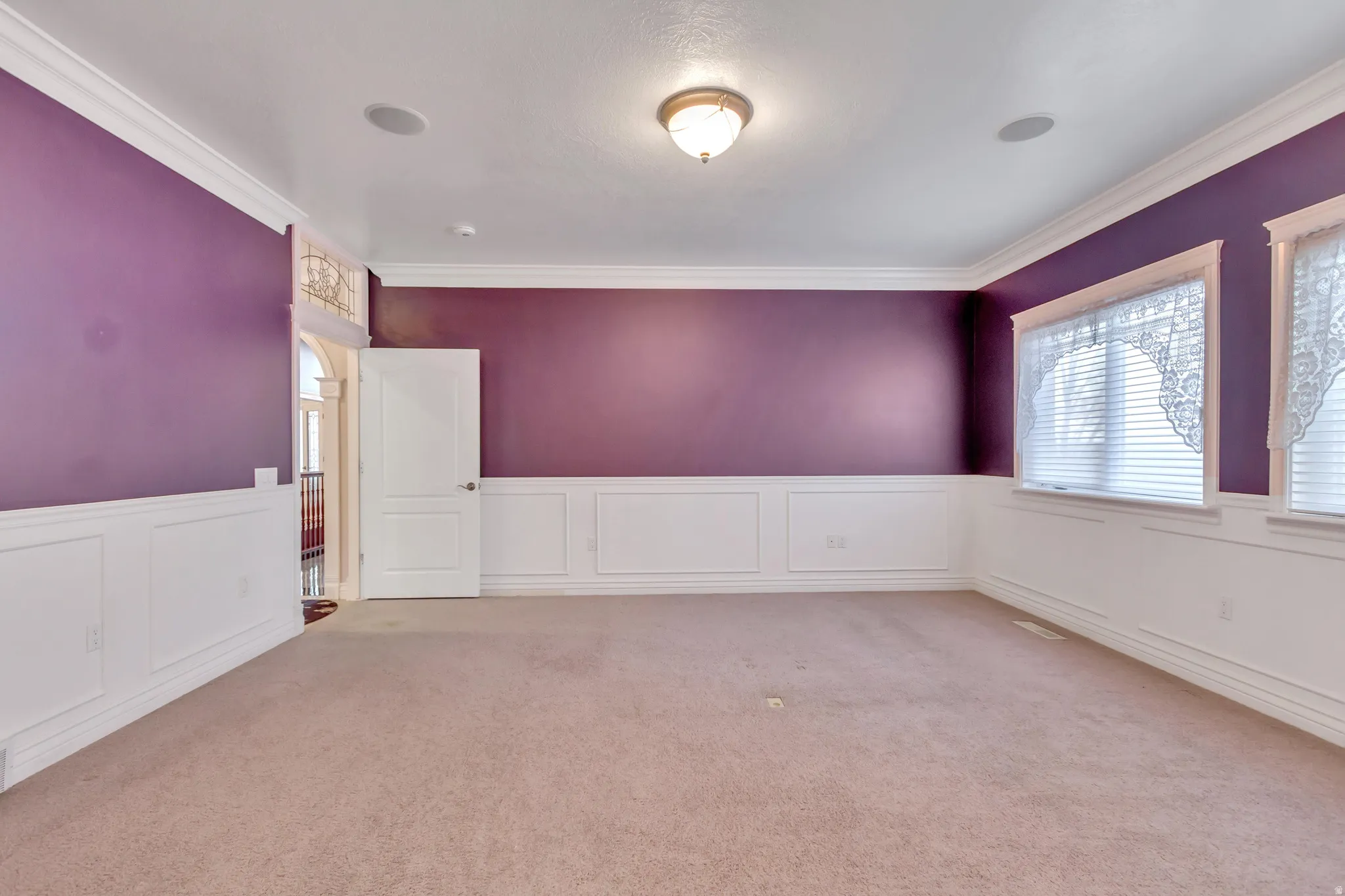 Spacious room featuring wainscoting, crown molding, and two windows with blinds