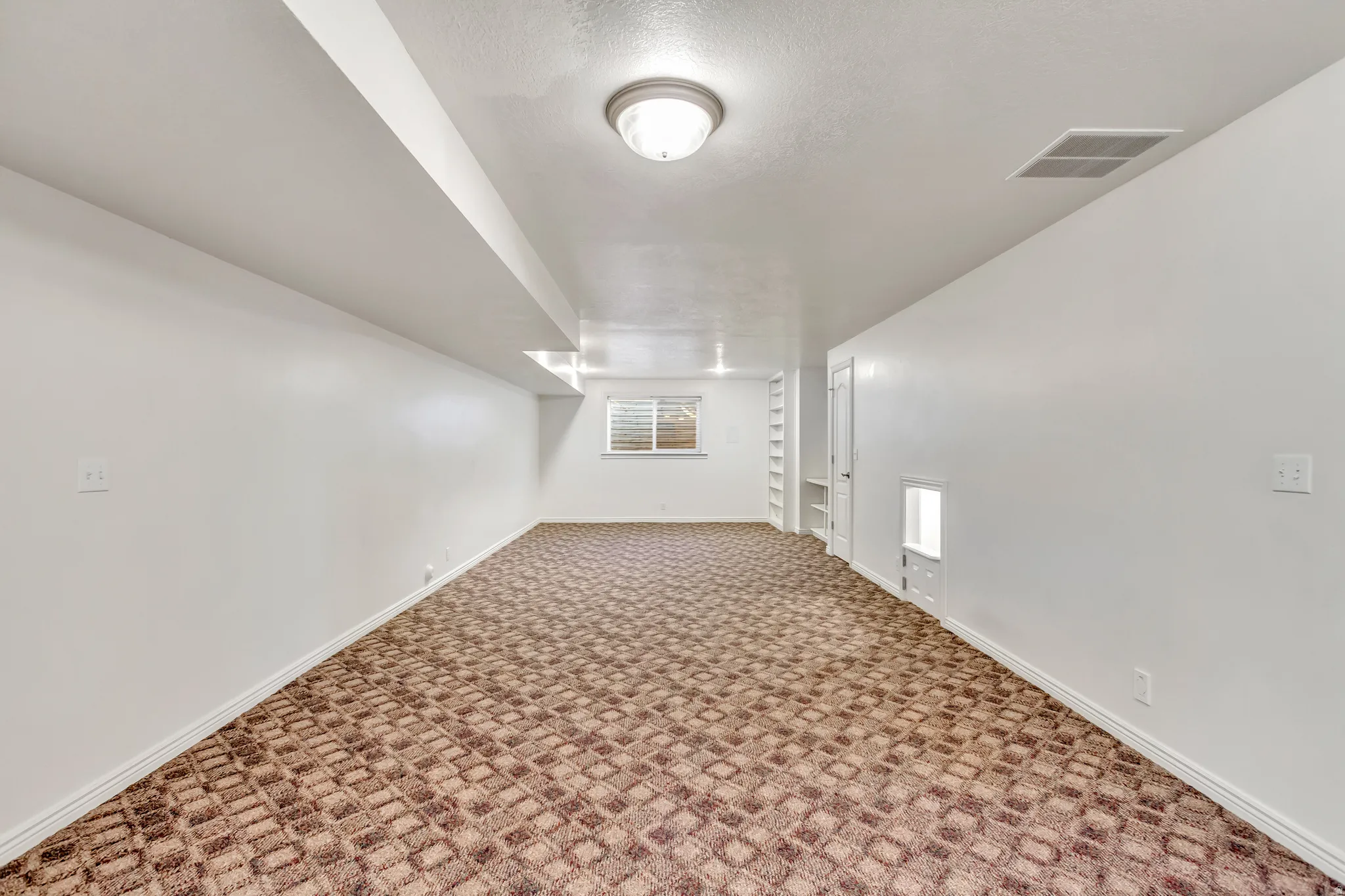 Spacious room featuring patterned carpet flooring, white painted walls, and a window with horizontal blinds
