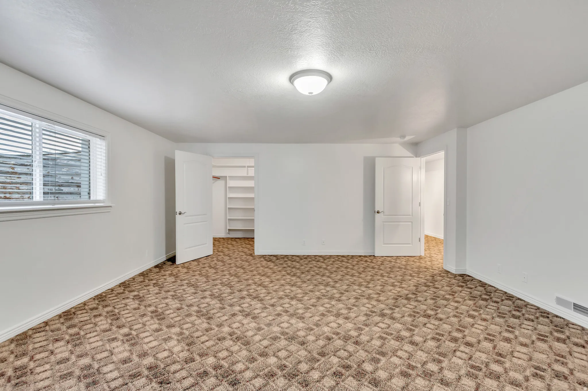 Spacious room featuring patterned carpet flooring, white walls, and a window with blinds