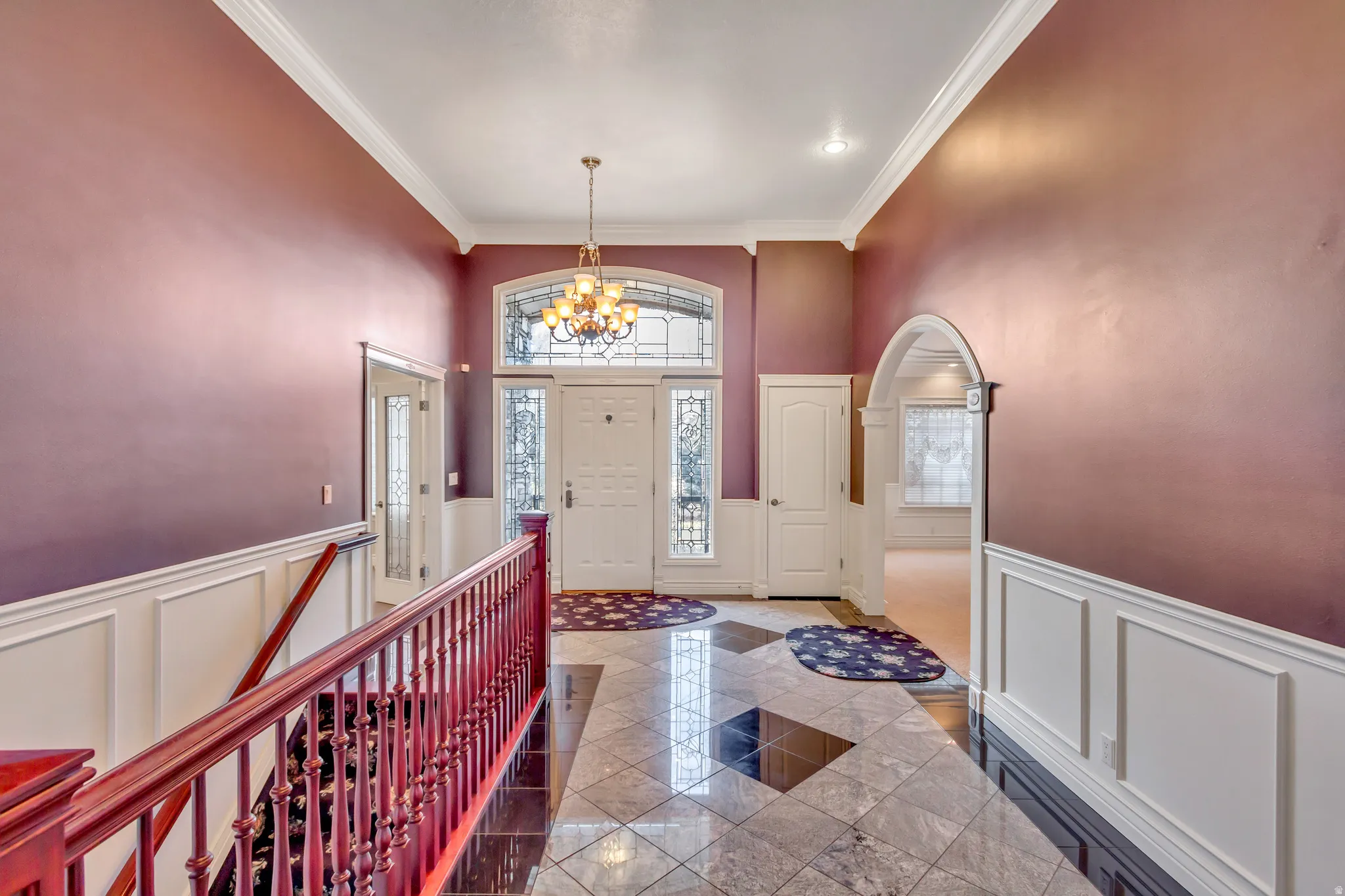 Grand entryway featuring a decorative chandelier, white paneled wainscoting, and a tiled floor with contrasting accents