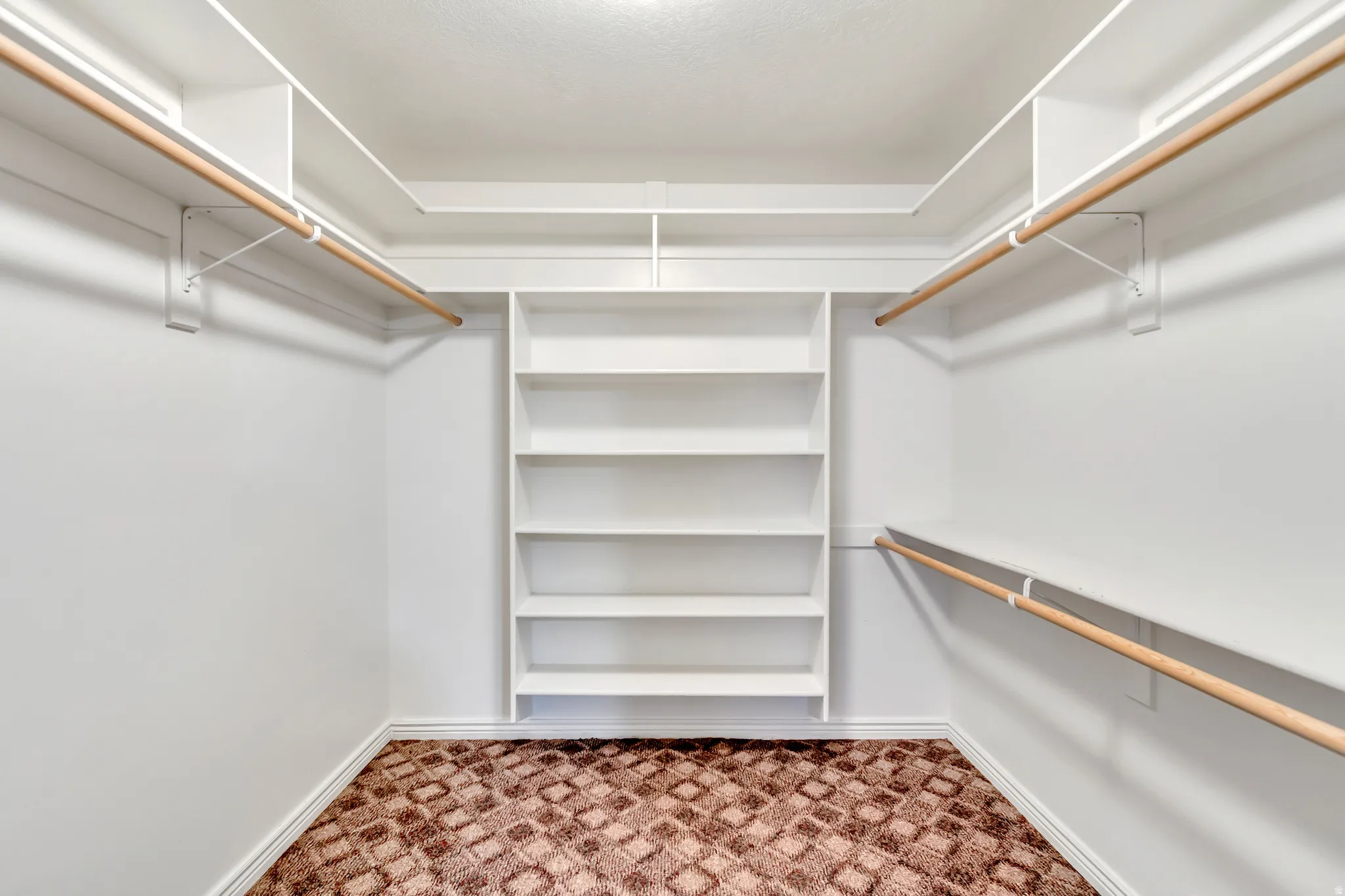 Walk-in closet featuring built-in shelving, dual hanging rods, white walls, white baseboards, and patterned carpet flooring