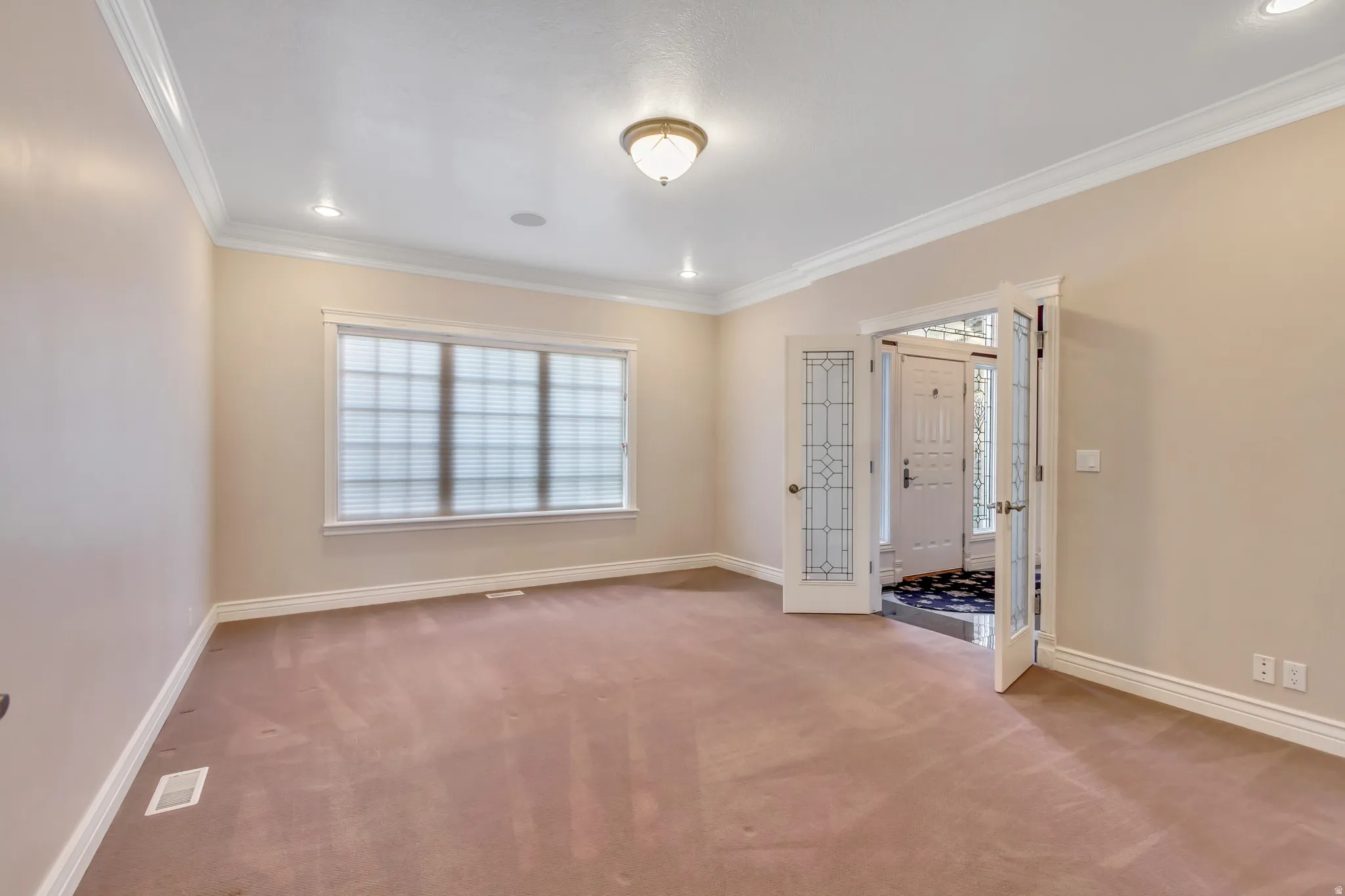 Spacious room featuring neutral wall paint, crown molding, recessed lighting, and a prominent window with blinds