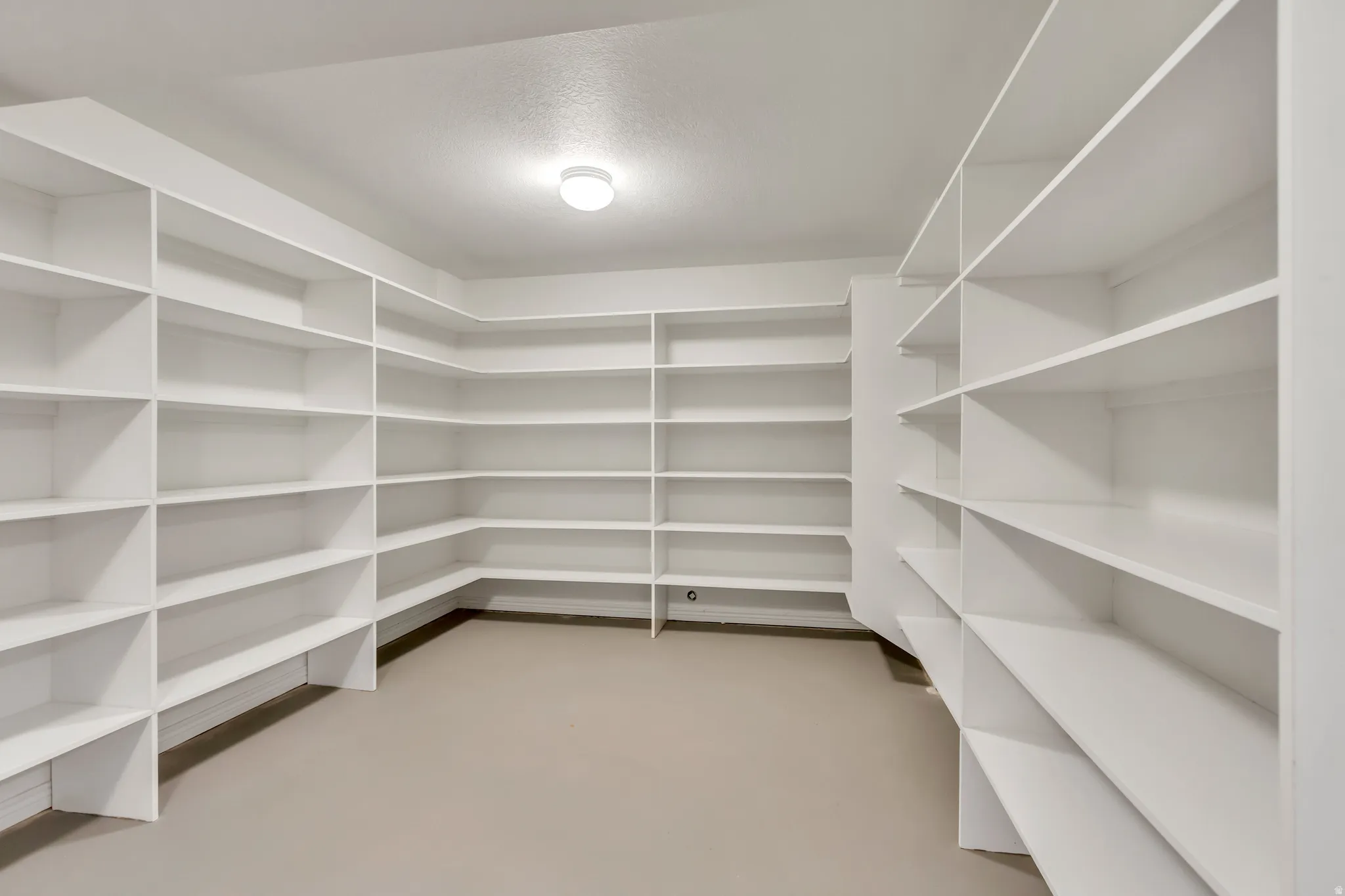 Spacious utility room featuring extensive built-in shelving, durable flooring, bright overhead lighting, and white walls