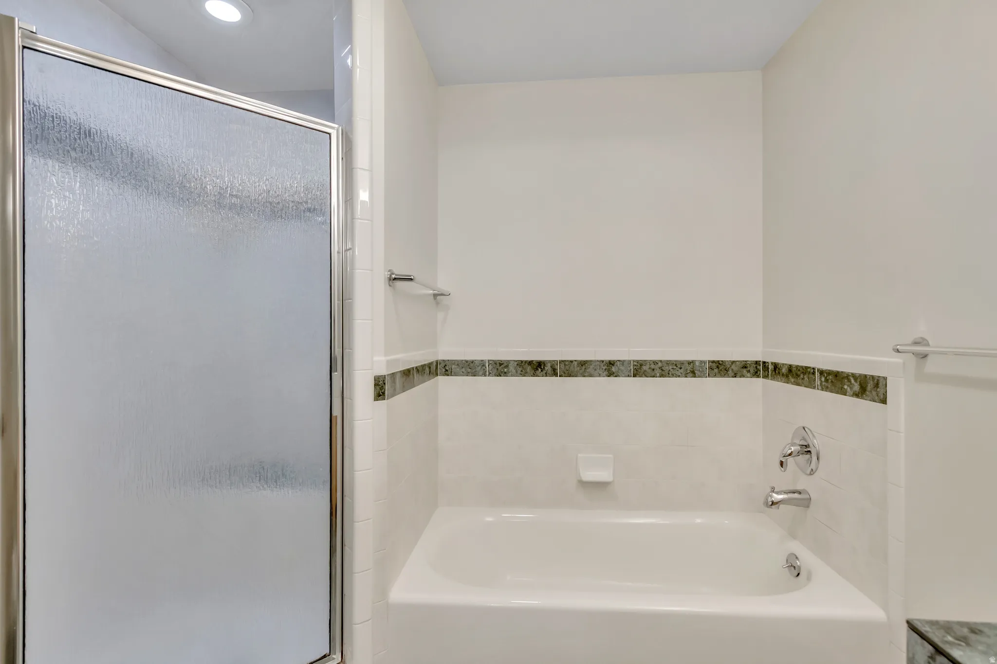 Shower-over-tub combination featuring a sliding glass door with a textured panel, chrome hardware, a tiled surround, a built-in soap dish, and a decorative tile accent band