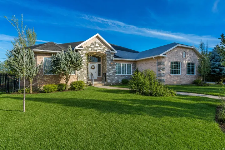 Spacious single-story residence featuring a stone and brick façade, a gabled entry with an arched portico, multiple window styles, a dark shingle roof, and a verdant front lawn