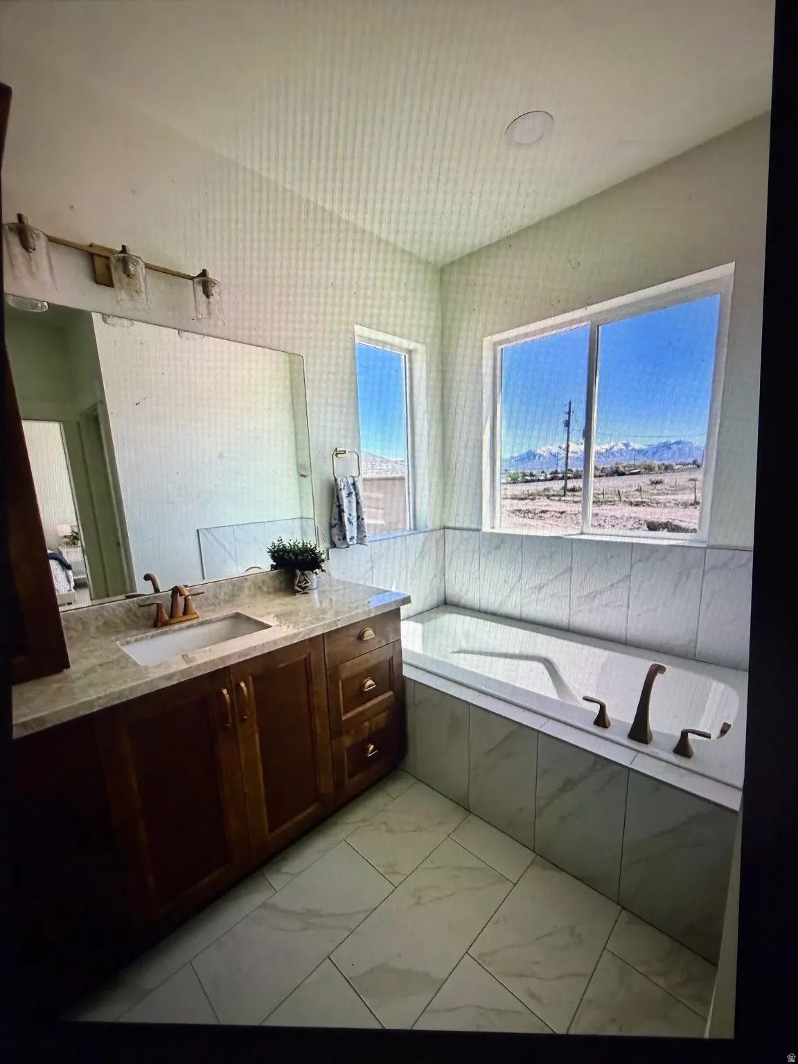 Built-in tub with tile surround, a spacious vanity with an undermount sink, and two large windows