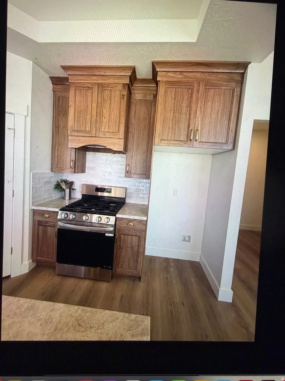 Kitchen featuring wood-finish cabinetry with crown molding, stainless steel range, light-toned backsplash, and stone-finish countertops