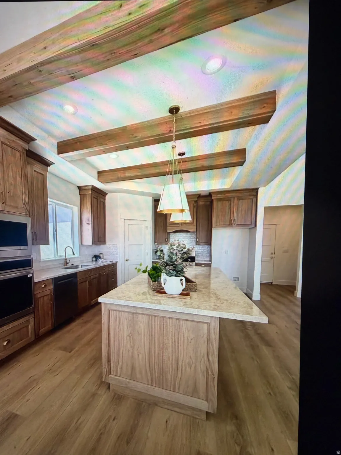 Kitchen featuring a central island with a light-toned countertop, wood-finish flooring, exposed wood ceiling beams, recessed lighting, and a pendant light fixture