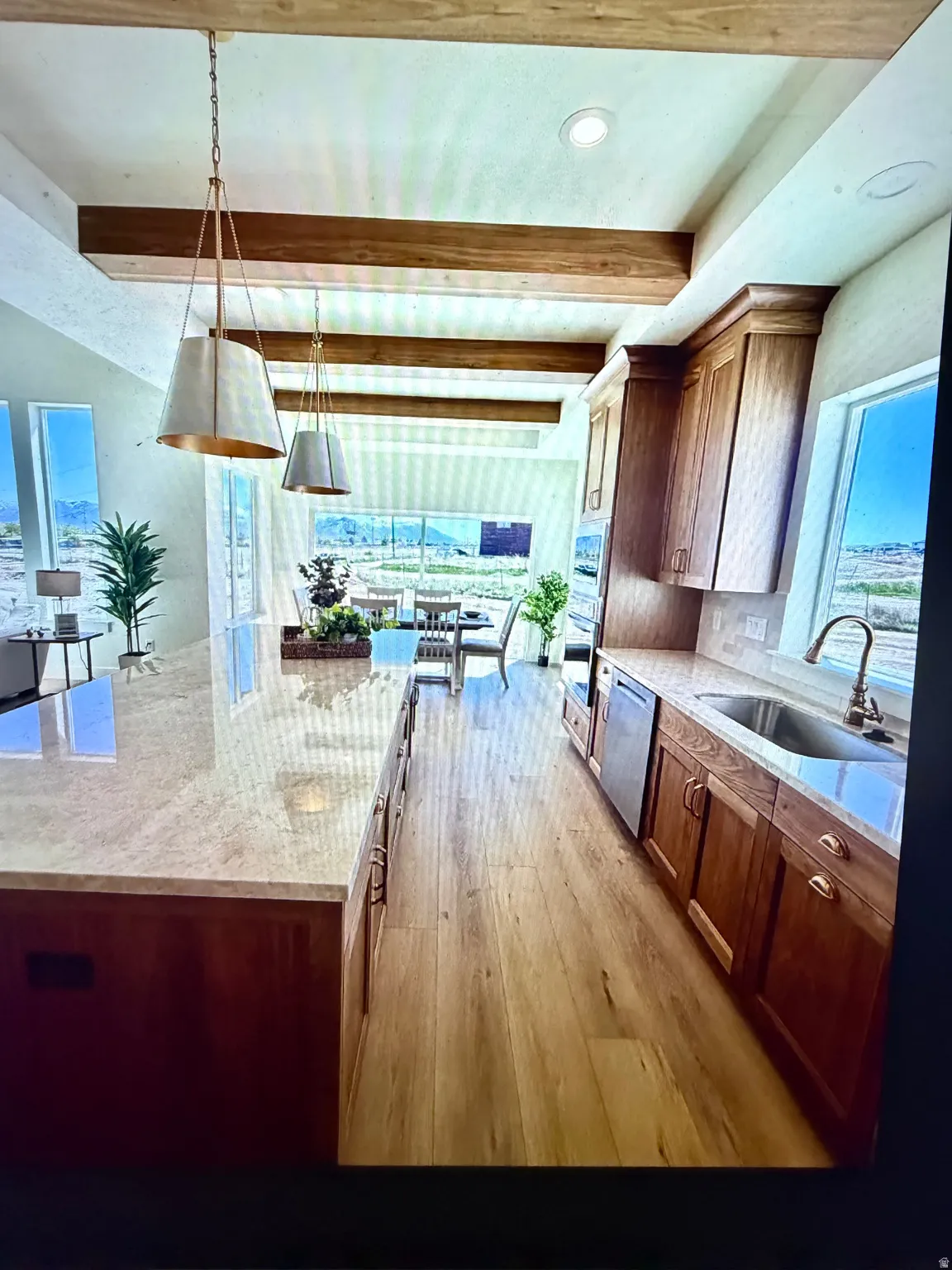 Gourmet kitchen featuring a large central island with light-toned countertop, wood-finish flooring, exposed ceiling beams, custom wood cabinetry, and pendant lighting