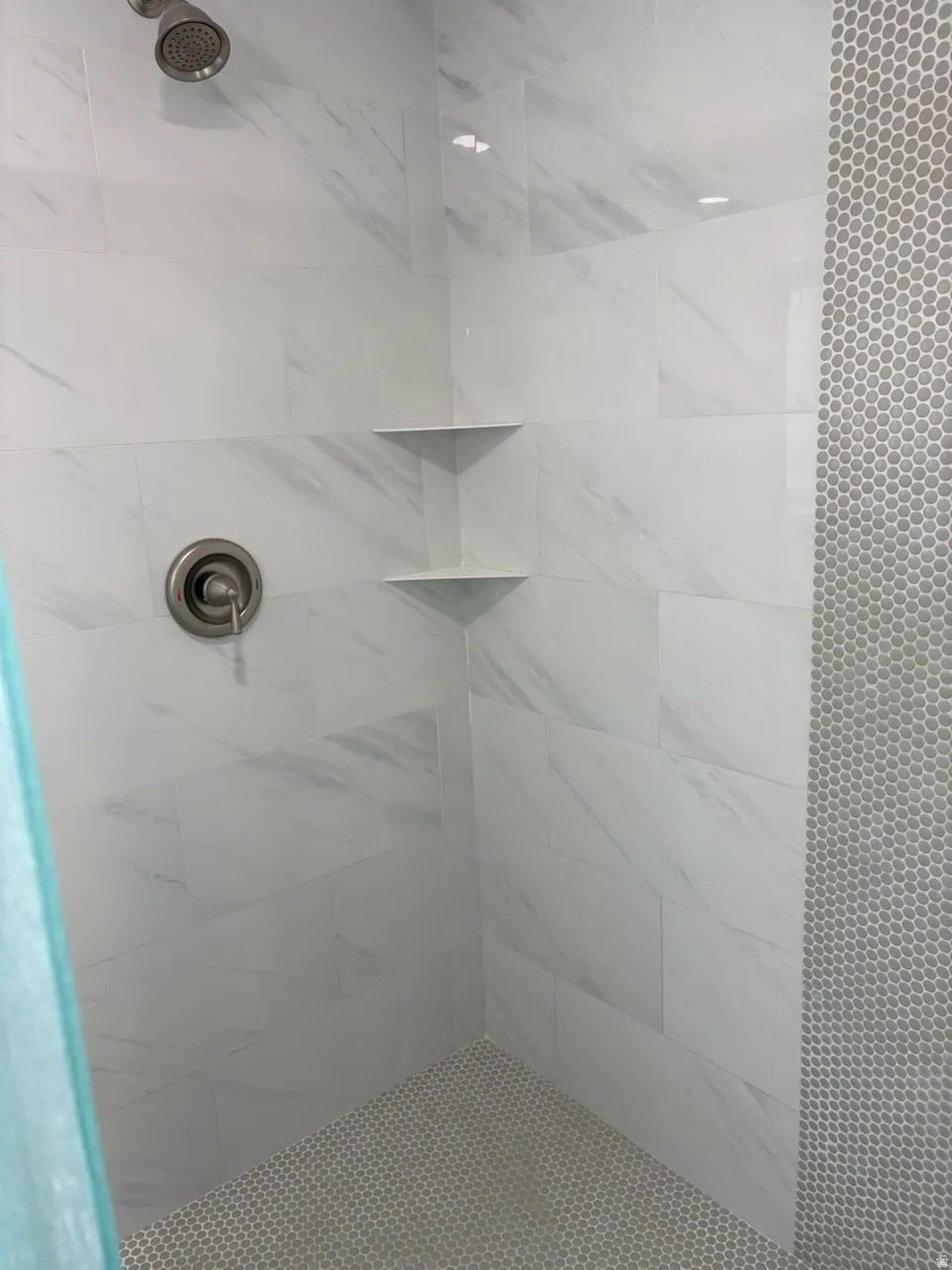 Shower with brushed nickel fixtures, large format white tile walls with subtle veining, and a hexagonal tile floor