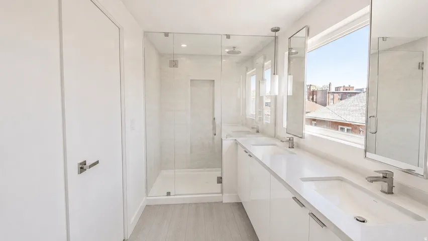 Contemporary bathroom featuring a dual vanity with undermount sinks, a spacious glass-enclosed shower, and light wood-finish flooring
