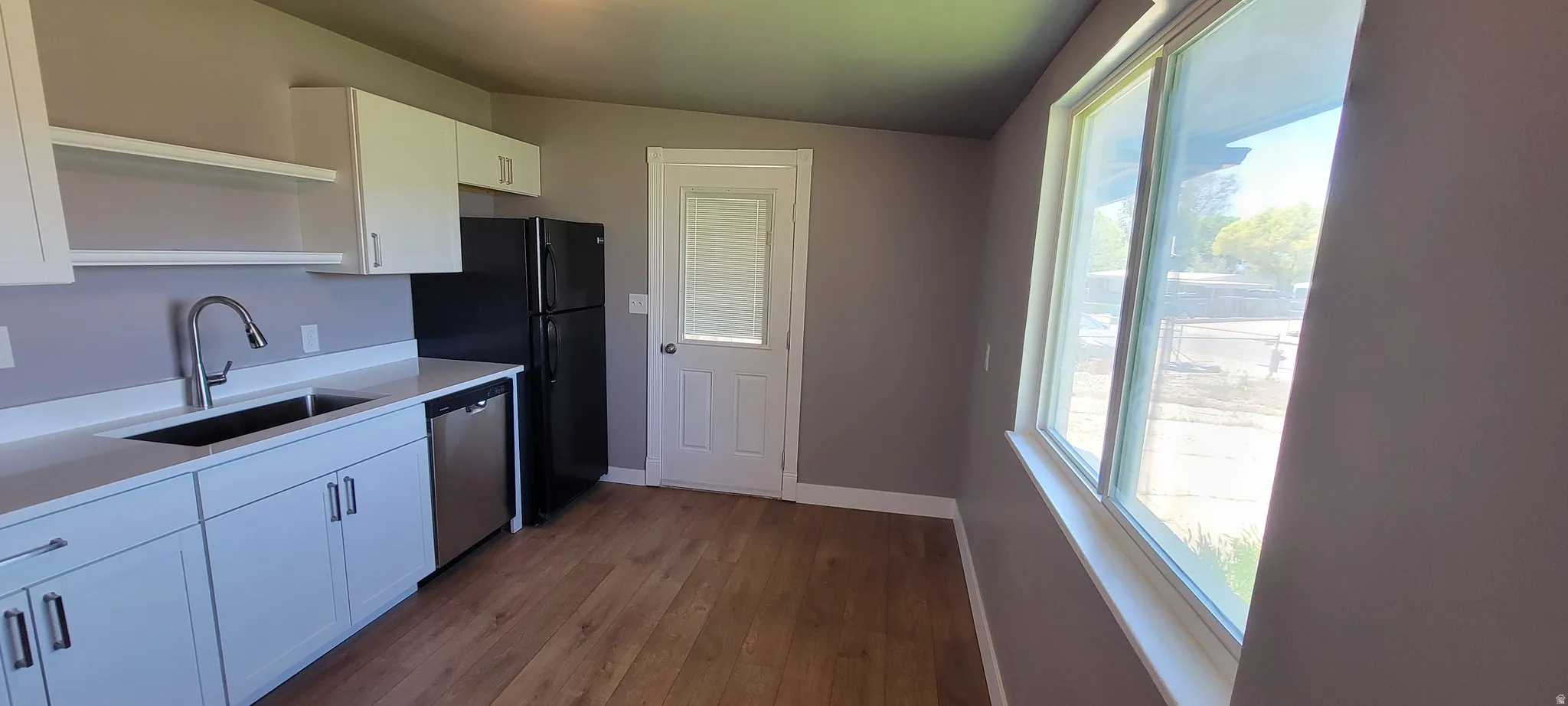 Kitchen featuring white cabinetry, a stainless steel dishwasher, a single basin sink with a gooseneck faucet, and wood-finish flooring