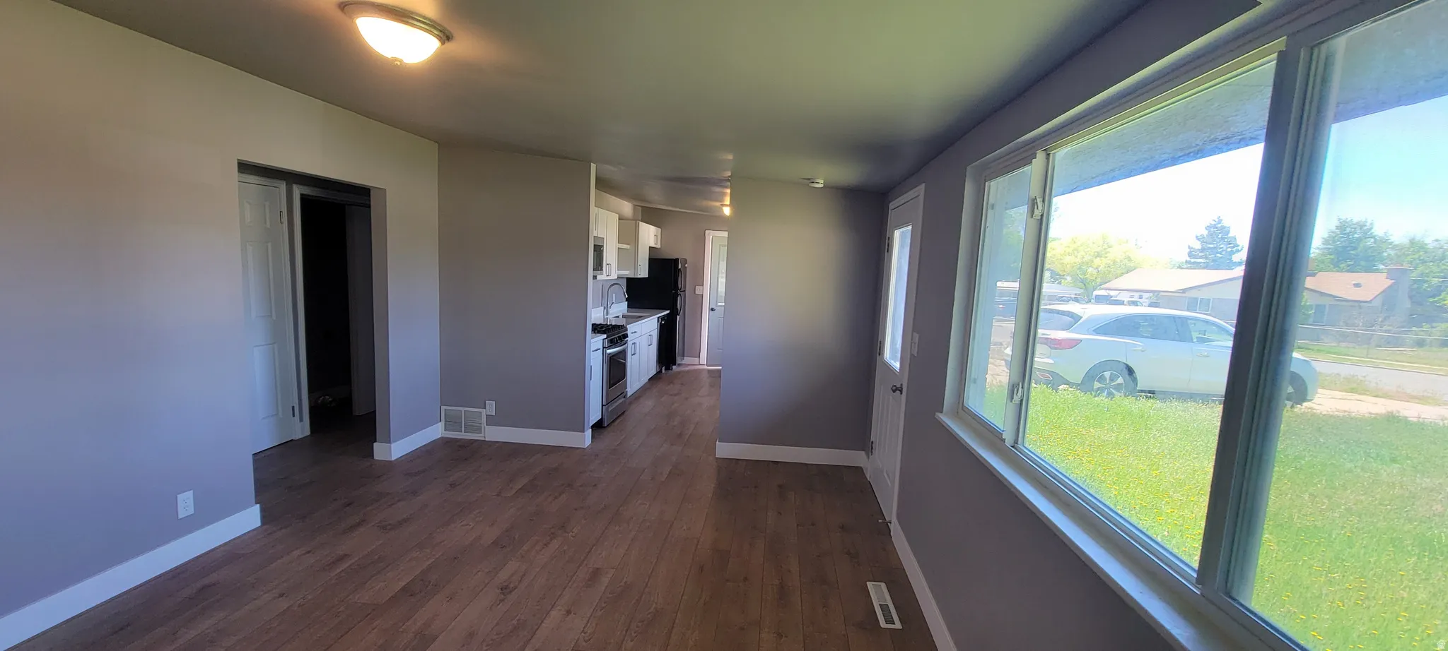 Open-concept living area featuring wood-finish flooring, neutral paint, a large window, and direct access to the kitchen area