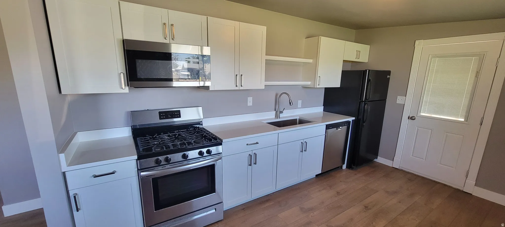 Full kitchen featuring white cabinetry, light countertops, stainless steel appliances, and wood-finish flooring