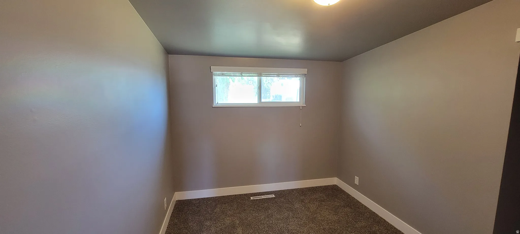 Room with neutral tone walls, dark carpet flooring, and white baseboards
