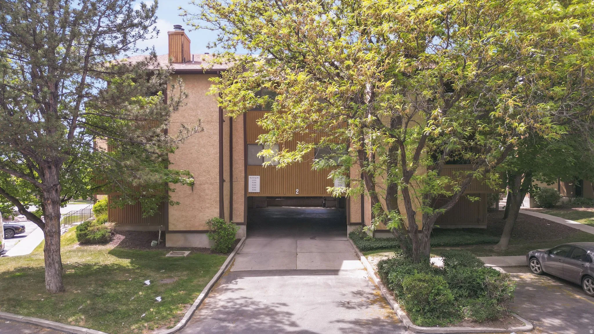 Multi-story building featuring stucco and wood-panel siding, a covered drive-through entryway, and mature landscaping