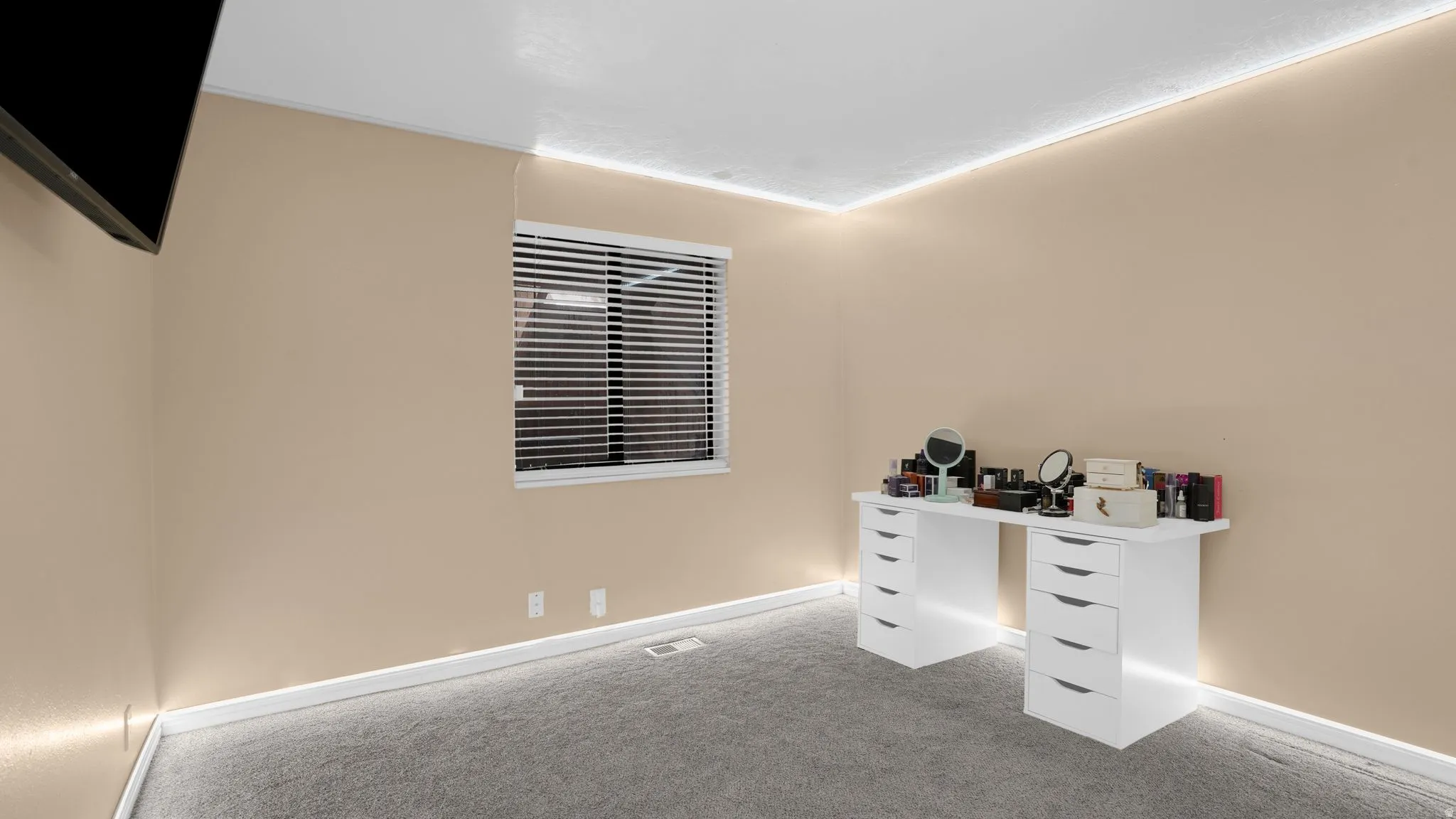 Wall-mounted television bracket, neutral wall paint, white window blinds, white baseboard trim, and gray carpet flooring