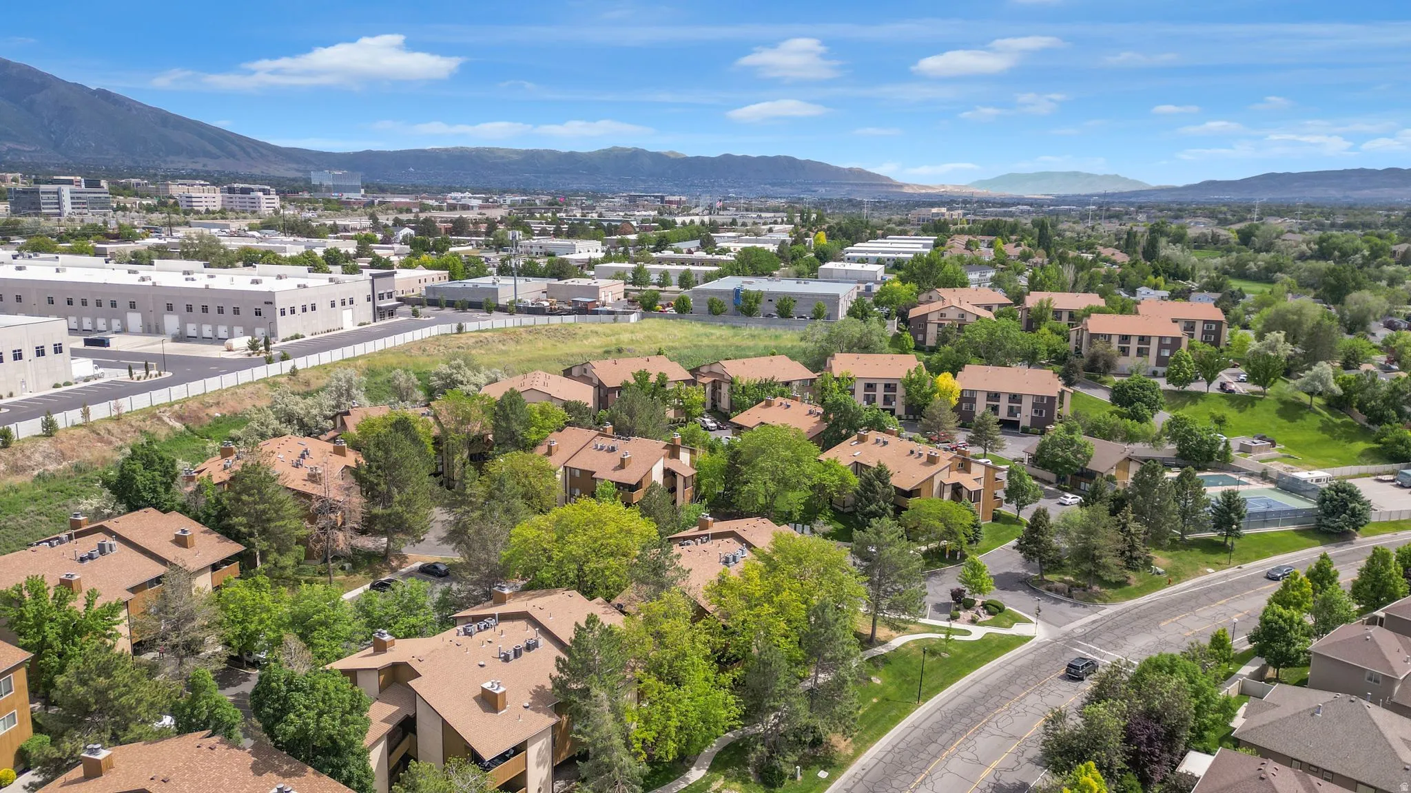 Community aerial showcasing residential buildings with terracotta-style roofs, surrounded by mature trees and manicured green spaces