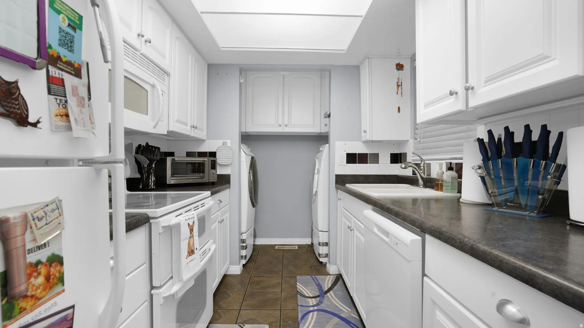 Galley kitchen with white cabinetry and dark countertops