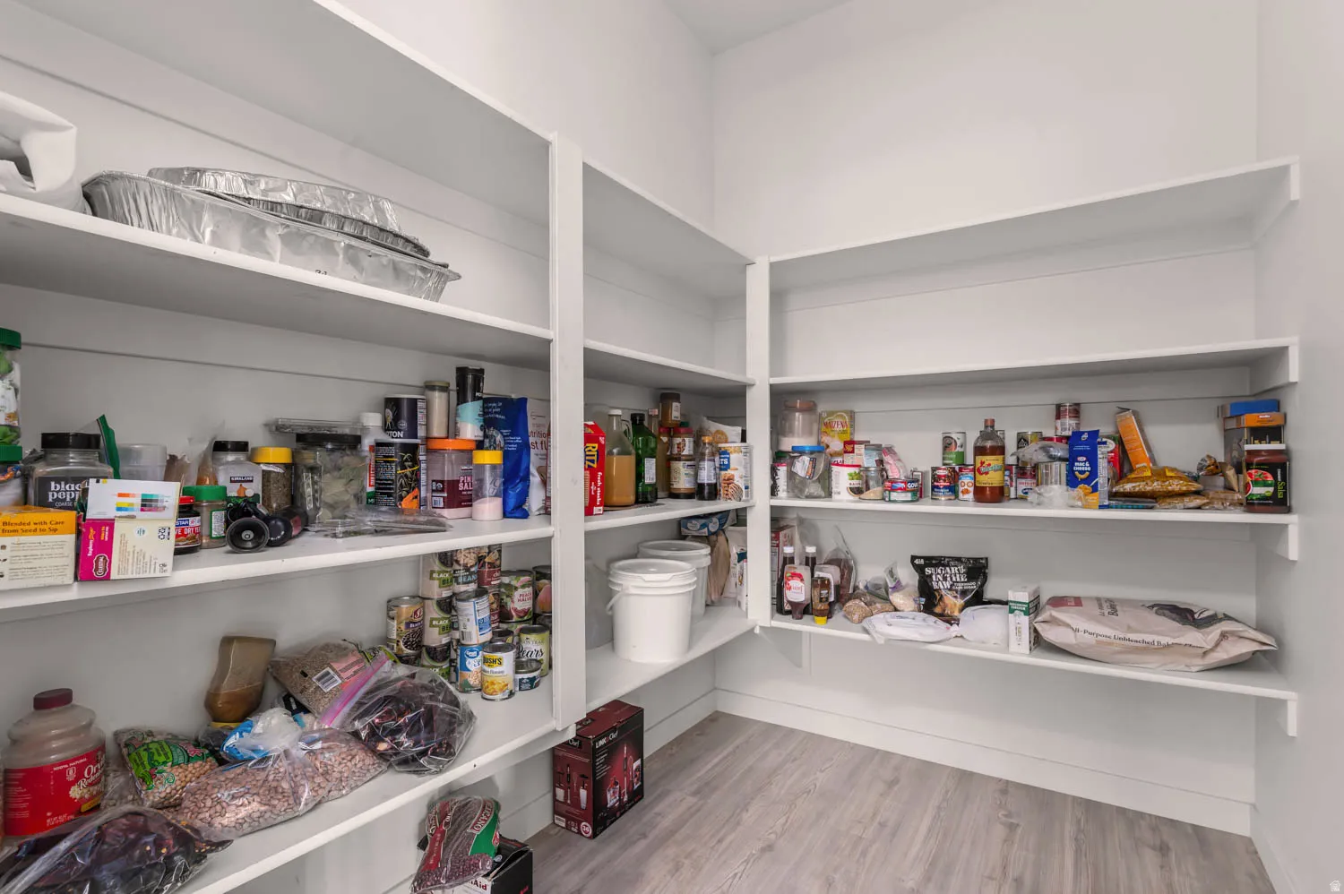 Spacious pantry featuring extensive built-in shelving, white walls, and wood-finish flooring