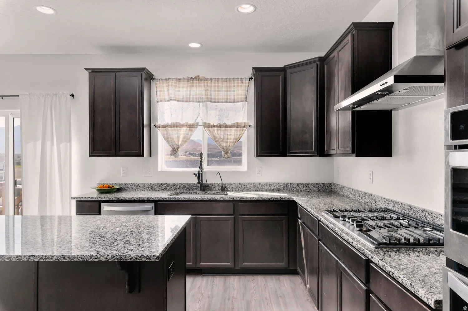 Modern kitchen featuring dark wood cabinetry, light-toned stone countertops, and wood-finish flooring