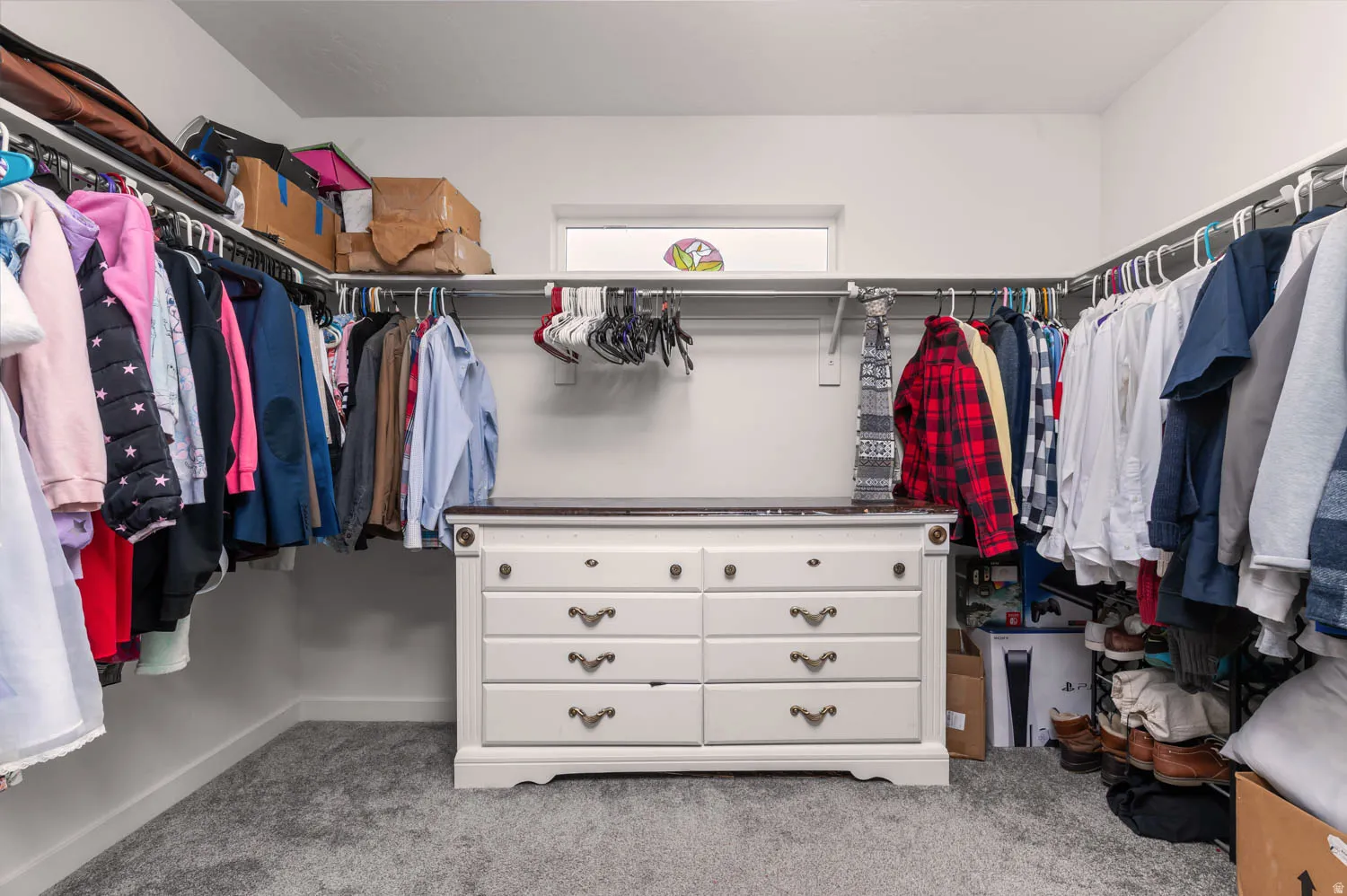 Spacious walk-in closet featuring white walls, gray carpet, and a built-in window providing natural light