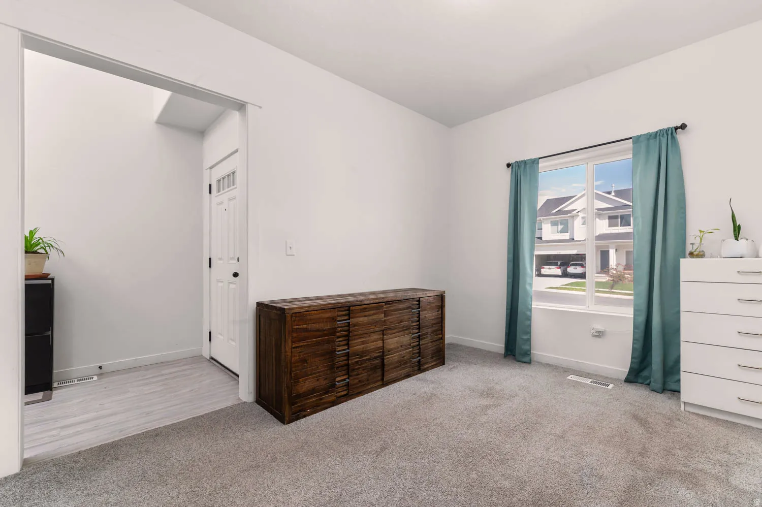 Spacious room featuring light gray carpeting, a large window with white trim, and a bright white paint scheme