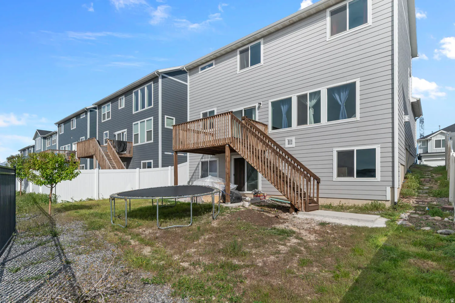 Rear exterior featuring light grey siding with white trim windows and a wooden deck with stairs providing access to the ground level