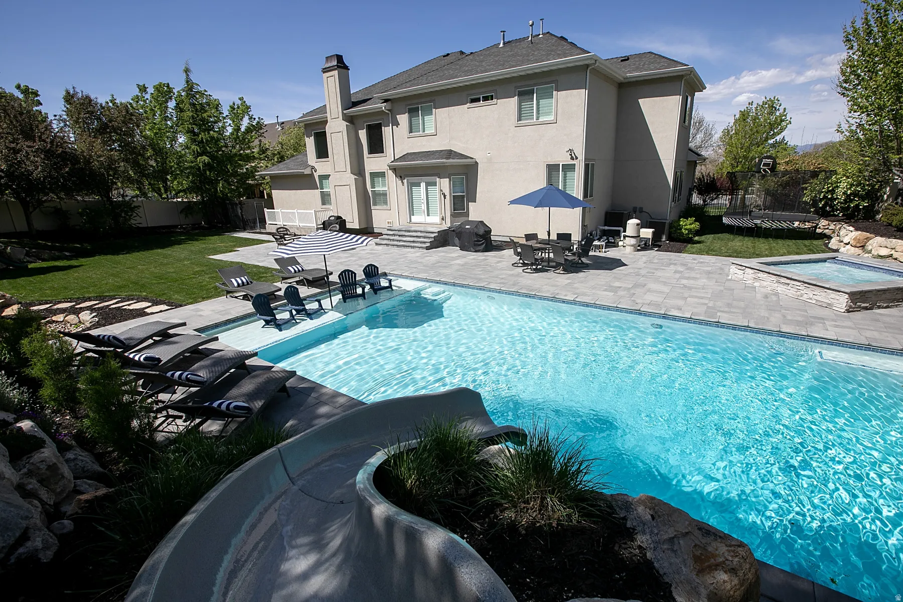 Expansive backyard featuring a large swimming pool with an integrated slide and a built-in spa