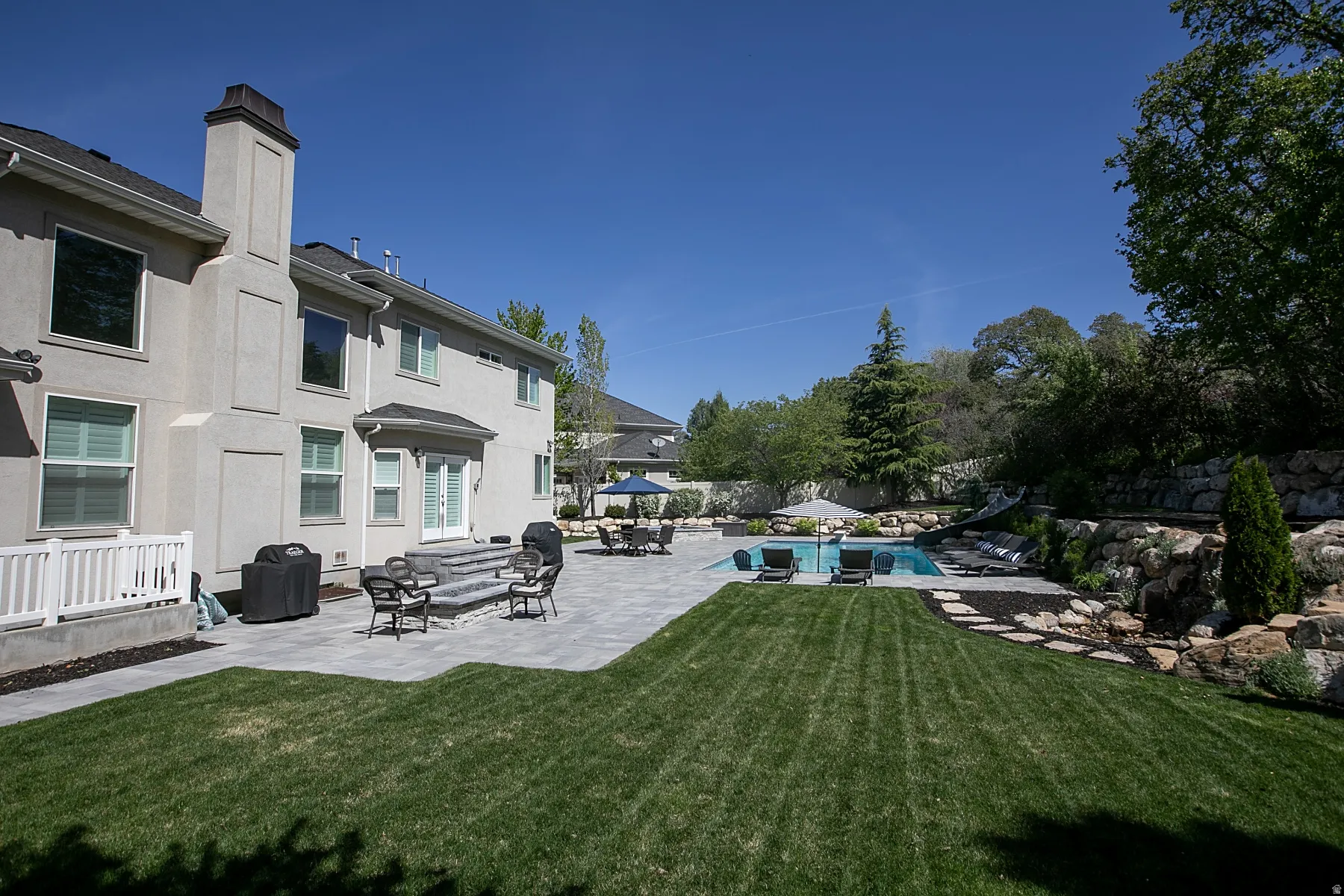 Expansive backyard featuring a rectangular swimming pool, paver patio, terraced landscaping with rock retaining walls, and a manicured lawn