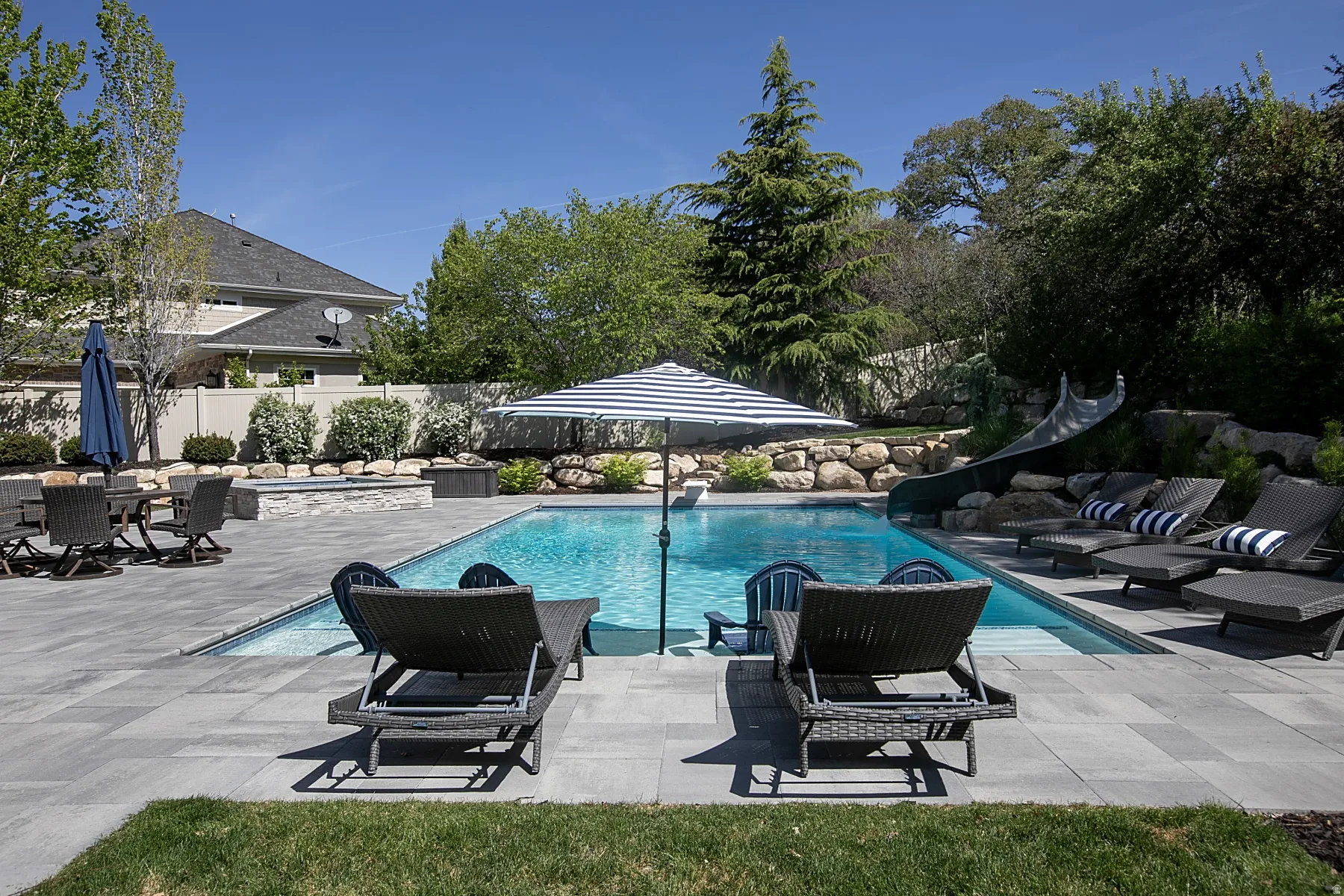 Outdoor pool featuring a built-in slide, extensive paver patio, and integrated spa