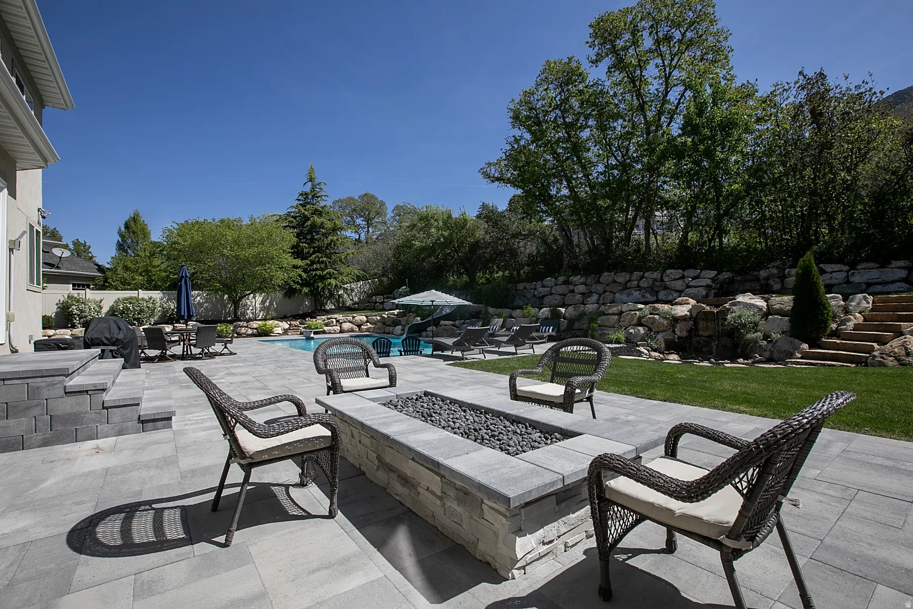 Expansive outdoor patio featuring a built-in fire pit, stone paver flooring, and a swimming pool