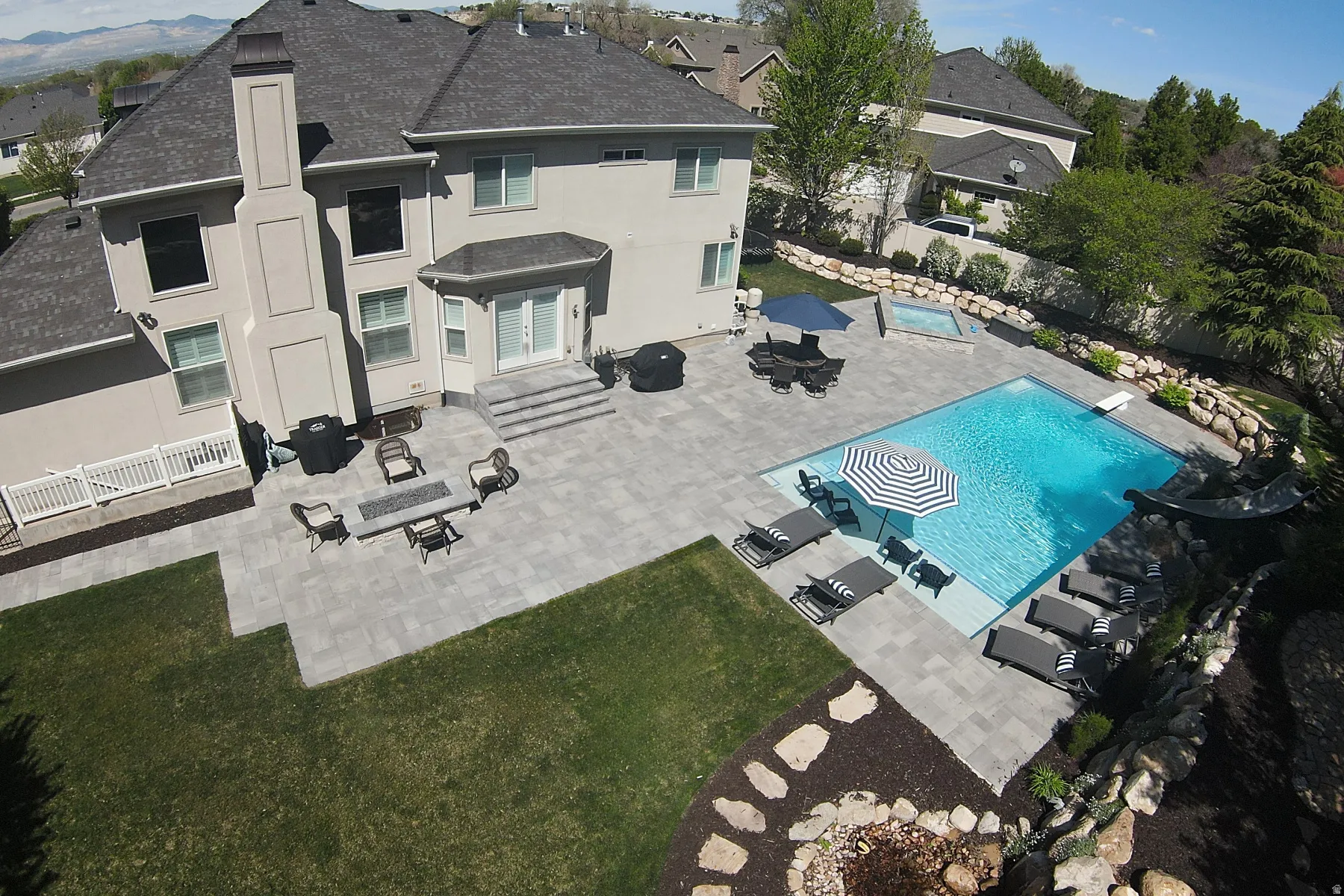 Expansive backyard featuring a large swimming pool, integrated hot tub, extensive paver patio, and terraced landscaping
