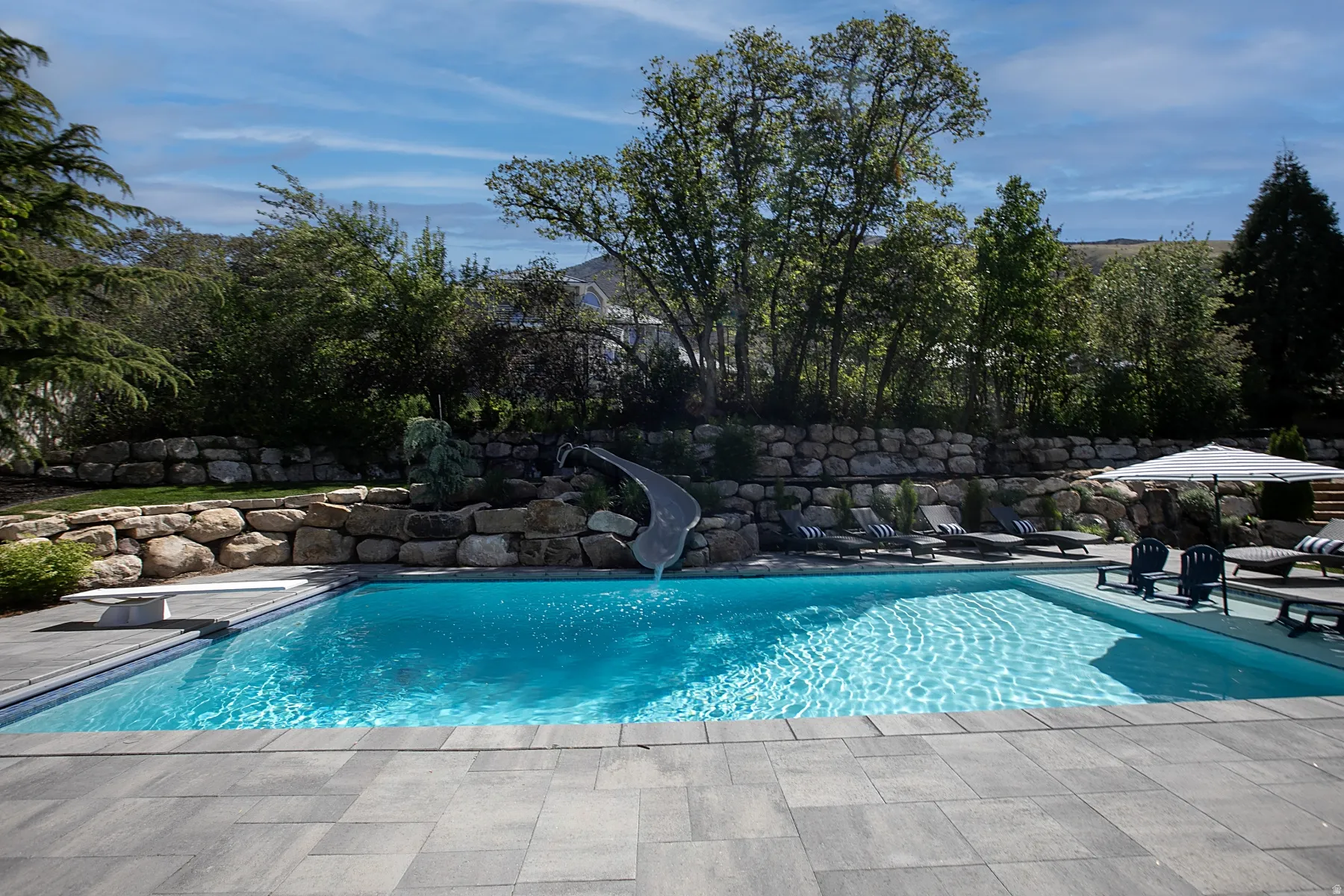 Rectangular swimming pool featuring a diving board, integrated slide, and surrounding stone patio