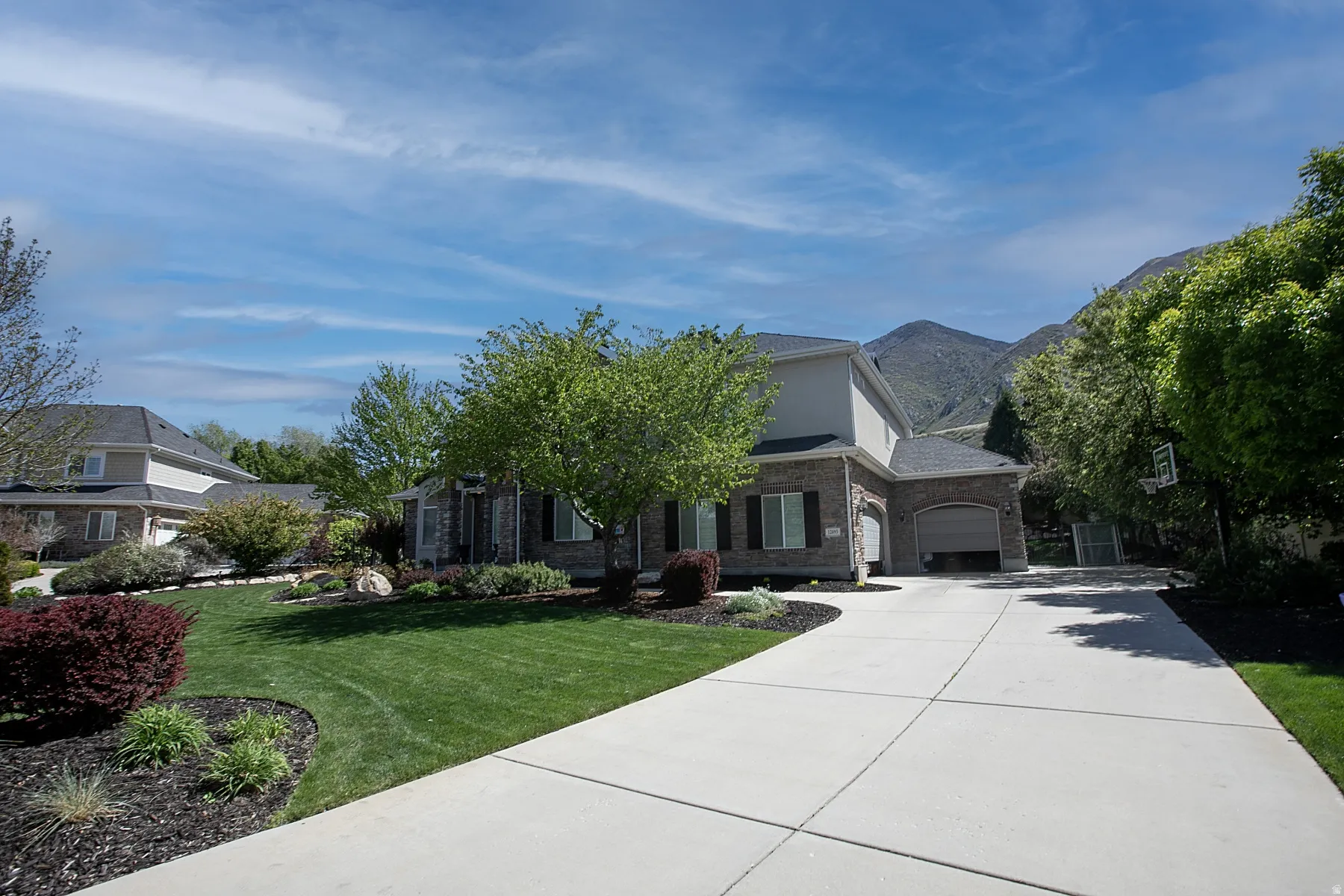 Brick and siding exterior featuring a two-car garage, mature trees, manicured lawn, and a paved driveway