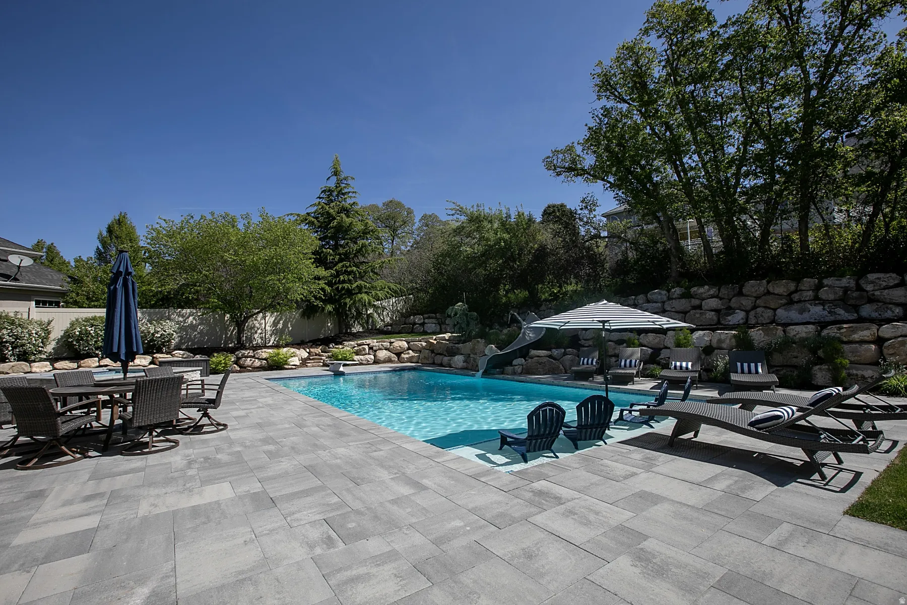 Expansive paver patio surrounding a rectangular swimming pool with integrated slide