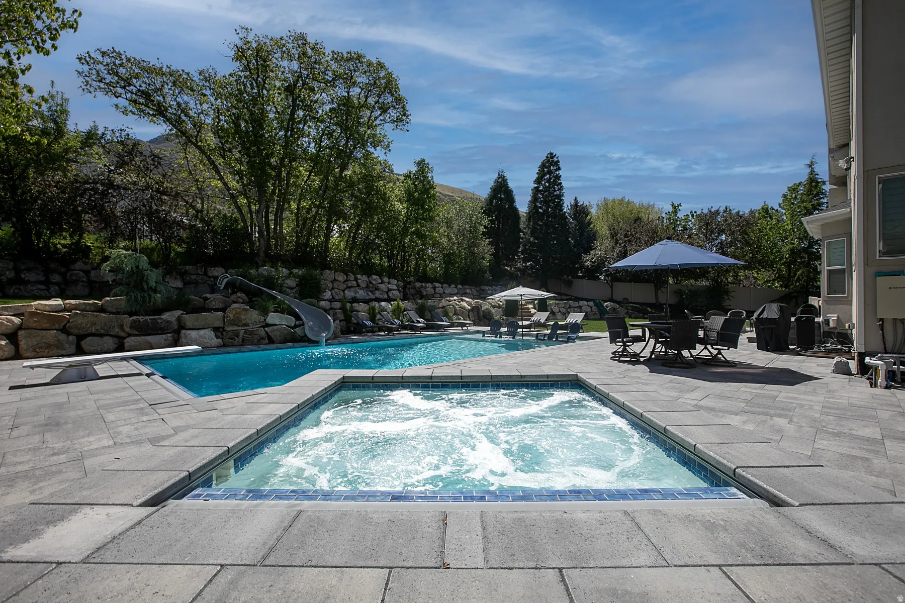 Outdoor living space featuring a large swimming pool with a diving board and slide, an integrated hot tub, and an expansive paver patio