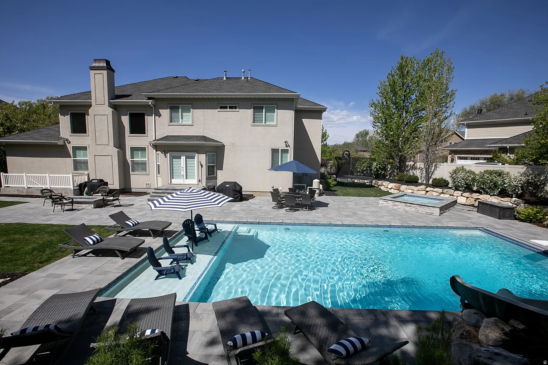 Expansive backyard featuring a rectangular swimming pool with an integrated sun shelf, a raised spa, and a pool slide