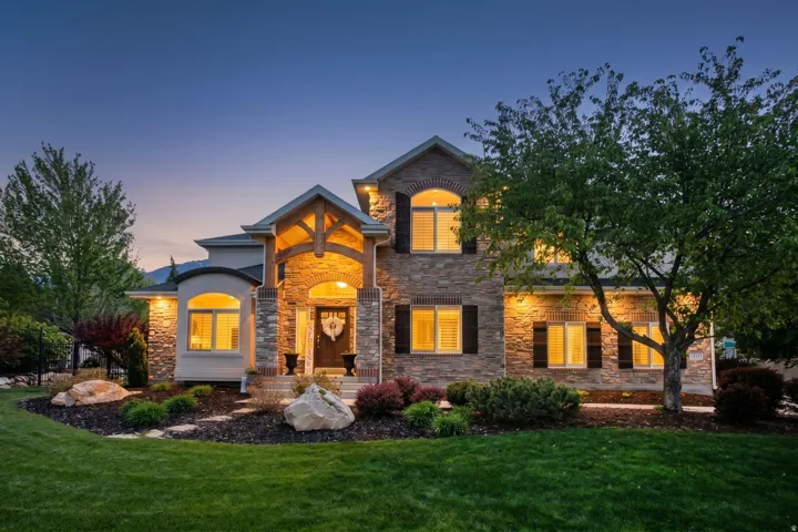 Stone and brick façade with arched entryway, dark wood shutters, and illuminated architectural elements