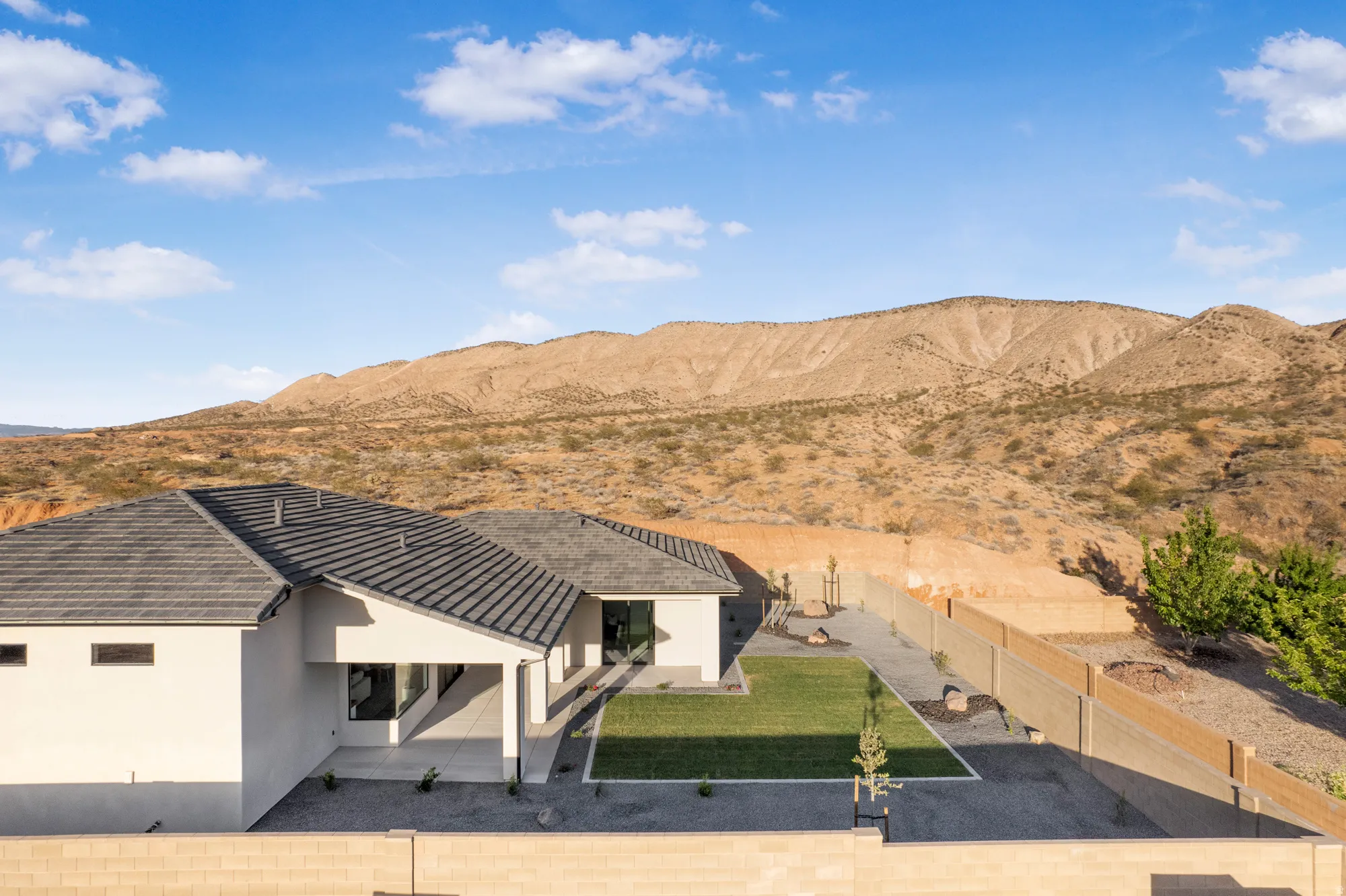 Rear exterior featuring a covered patio, manicured lawn, and low-maintenance landscaping, framed by a concrete block fence and desert mountain backdrop
