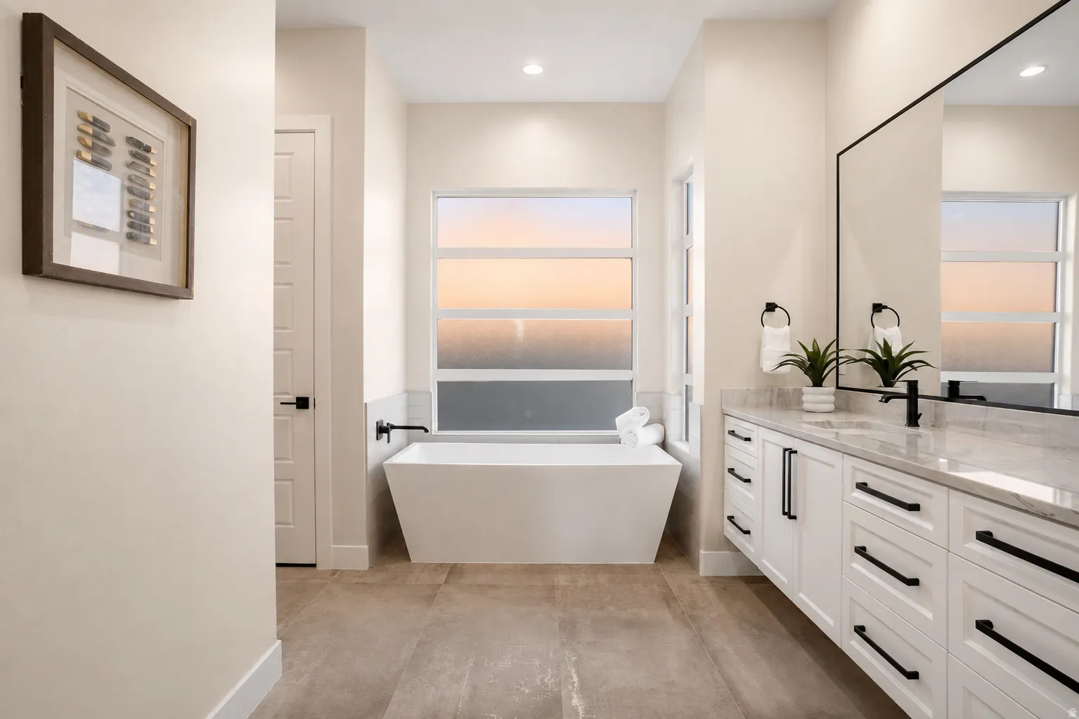 Bathroom featuring a freestanding soaking tub, dual-sink vanity with stone countertop, large rectangular mirror, and matte black fixtures