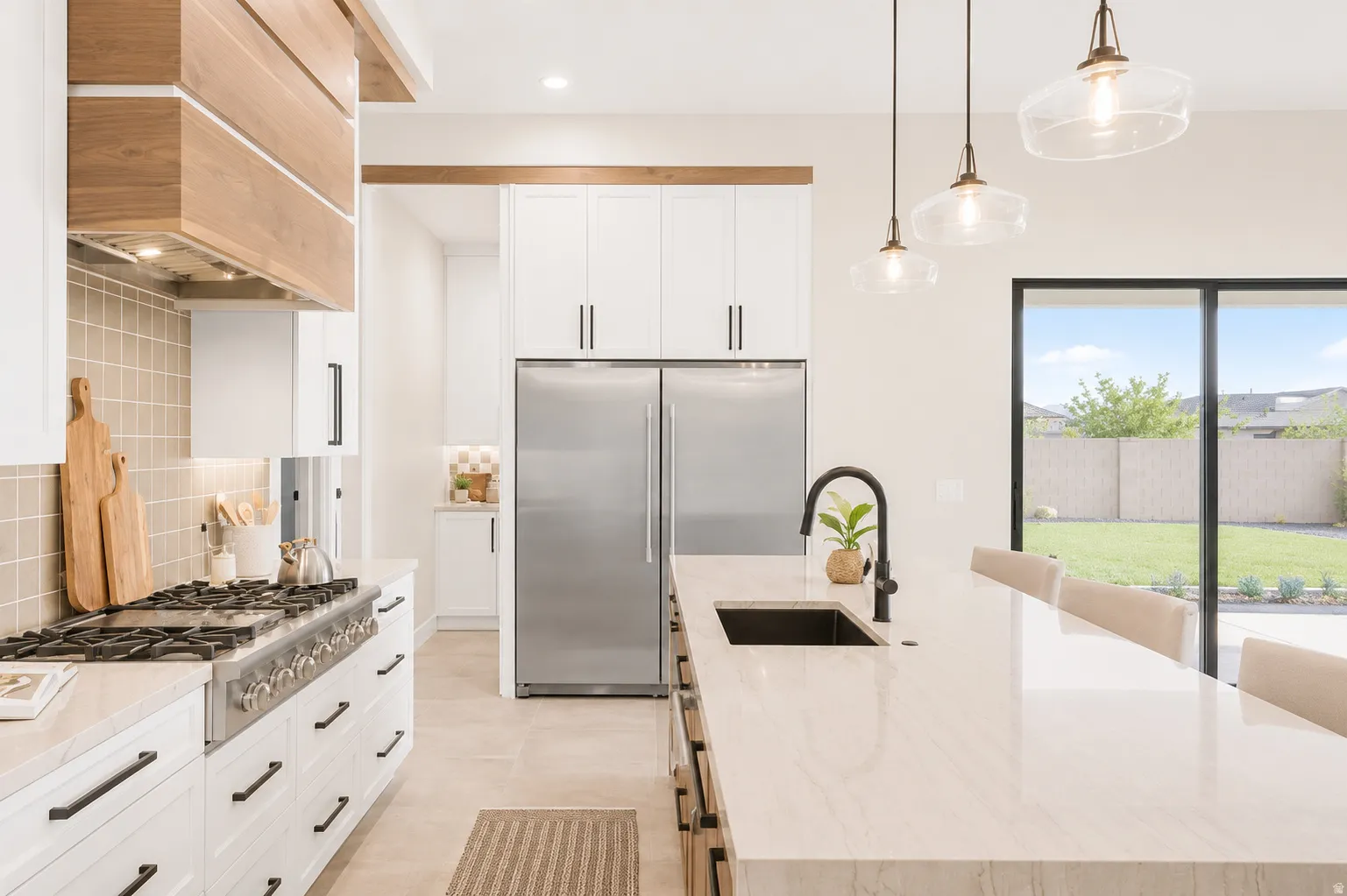 Gourmet kitchen with a large central island, professional-grade gas range, built-in stainless steel refrigerator, white cabinetry, and wood-finish range hood