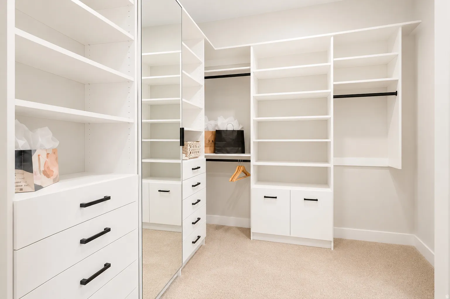 Custom built-in white cabinetry featuring multiple shelving units, integrated drawers with dark hardware, a full-length mirrored door, and black hanging rods
