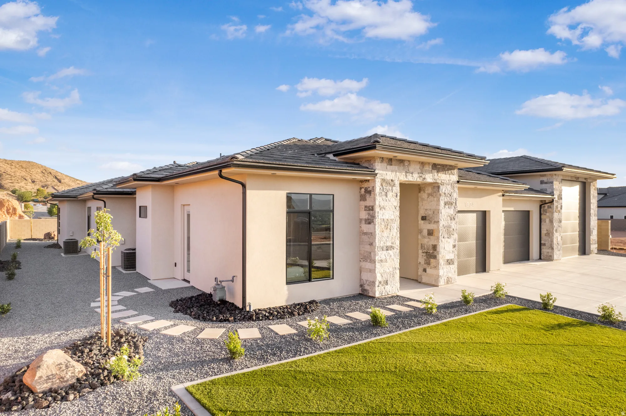 Contemporary exterior featuring stucco siding, stone accents, a dark tile roof, and a three-car garage