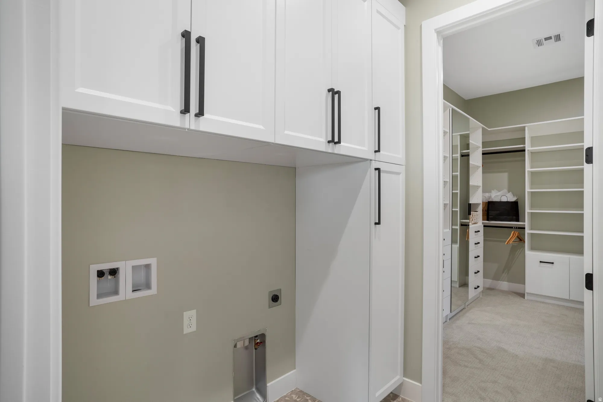 Laundry area featuring white cabinetry with matte black hardware