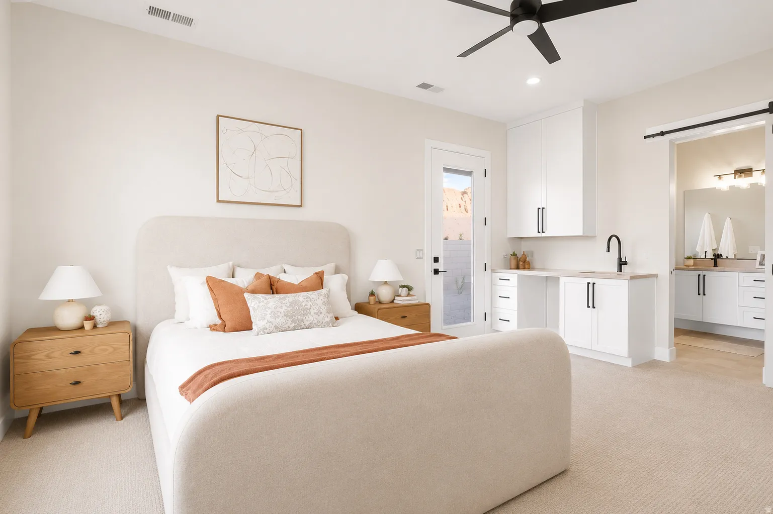 Spacious bedroom featuring light-toned carpeting, a ceiling fan, and a built-in wet bar with white cabinetry and a black faucet