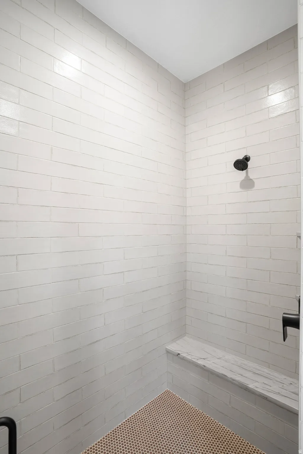 Shower stall featuring white subway tile, a built-in stone bench, a matte black shower head, and a coordinating matte black control handle