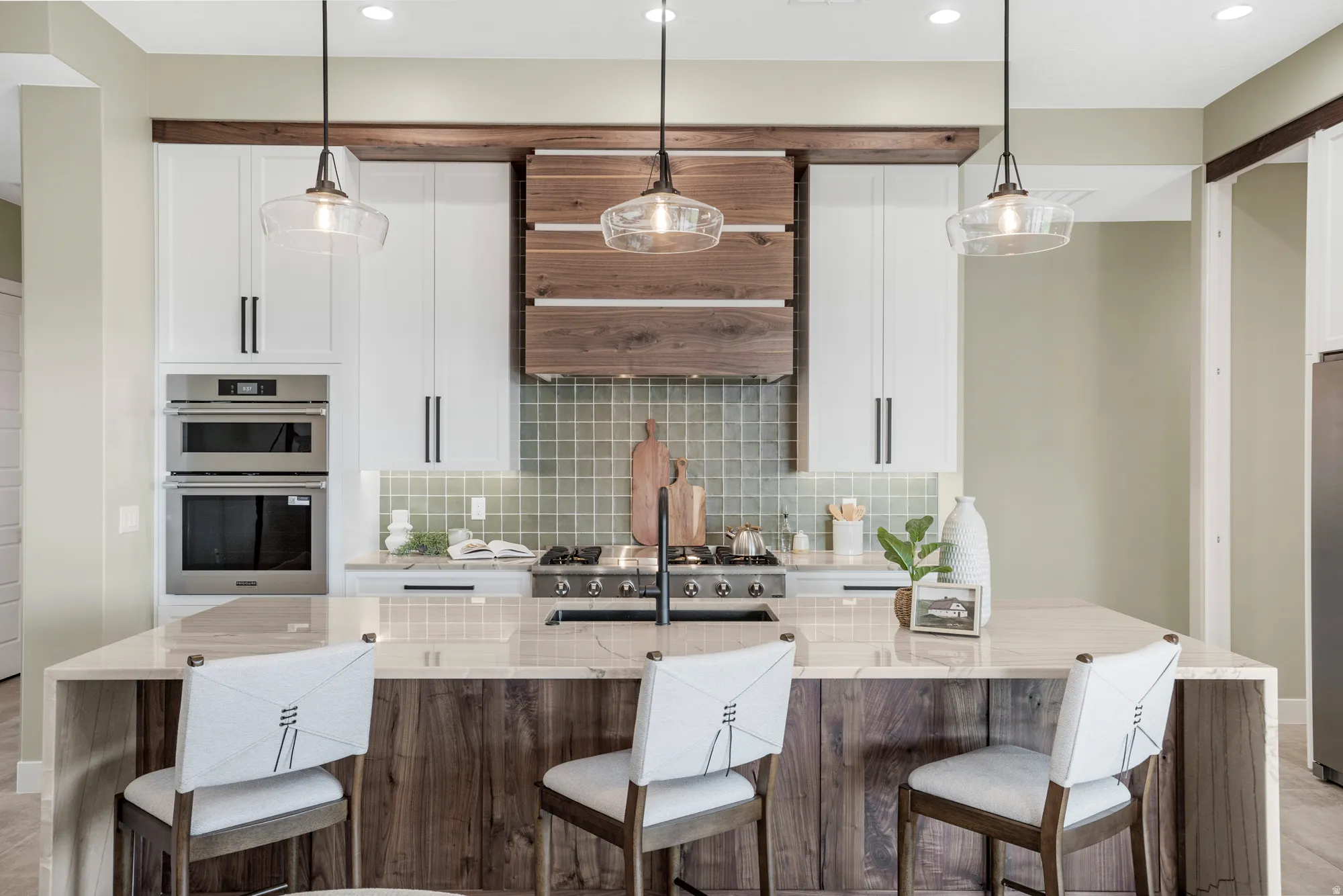 Kitchen featuring white cabinetry, stainless steel built-in appliances, a gas range, a multi-tone tile backsplash, and an island with wood-finish paneling and a light-toned countertop