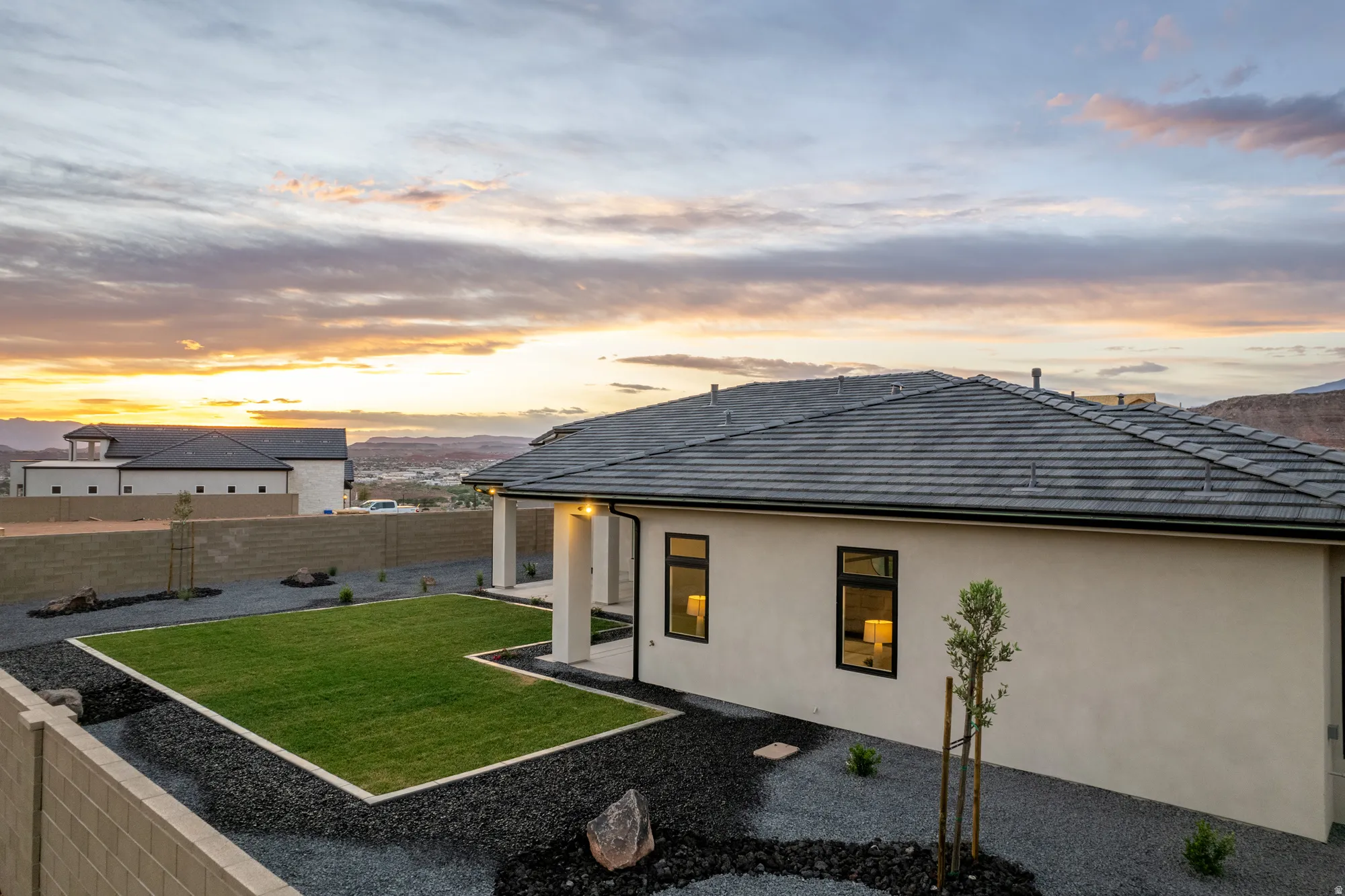 Contemporary stucco exterior with a dark tile roof, featuring a private backyard with a manicured lawn area and decorative gravel landscaping